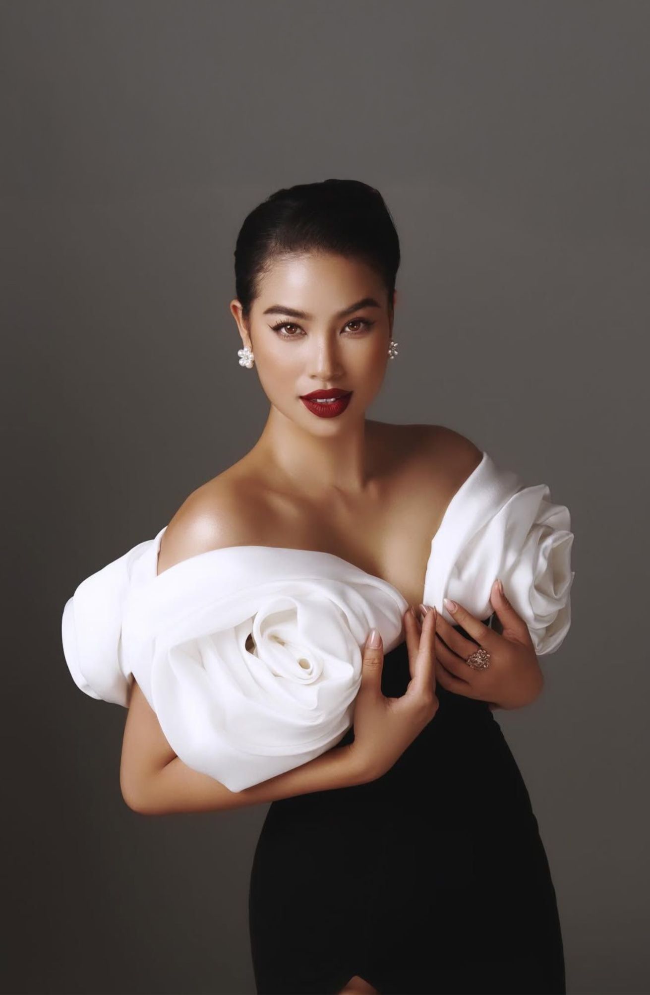 Modern maternity portrait in black dress holding white fabric against gray background.