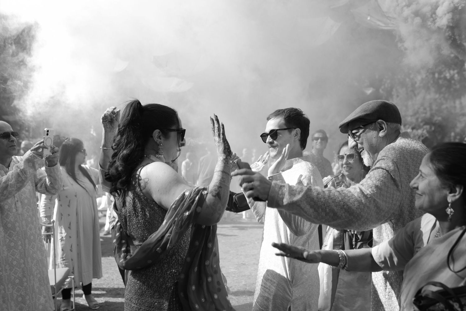 A group of people stand outdoors in black and white, surrounded by a cloud of smoke or mist in the air.