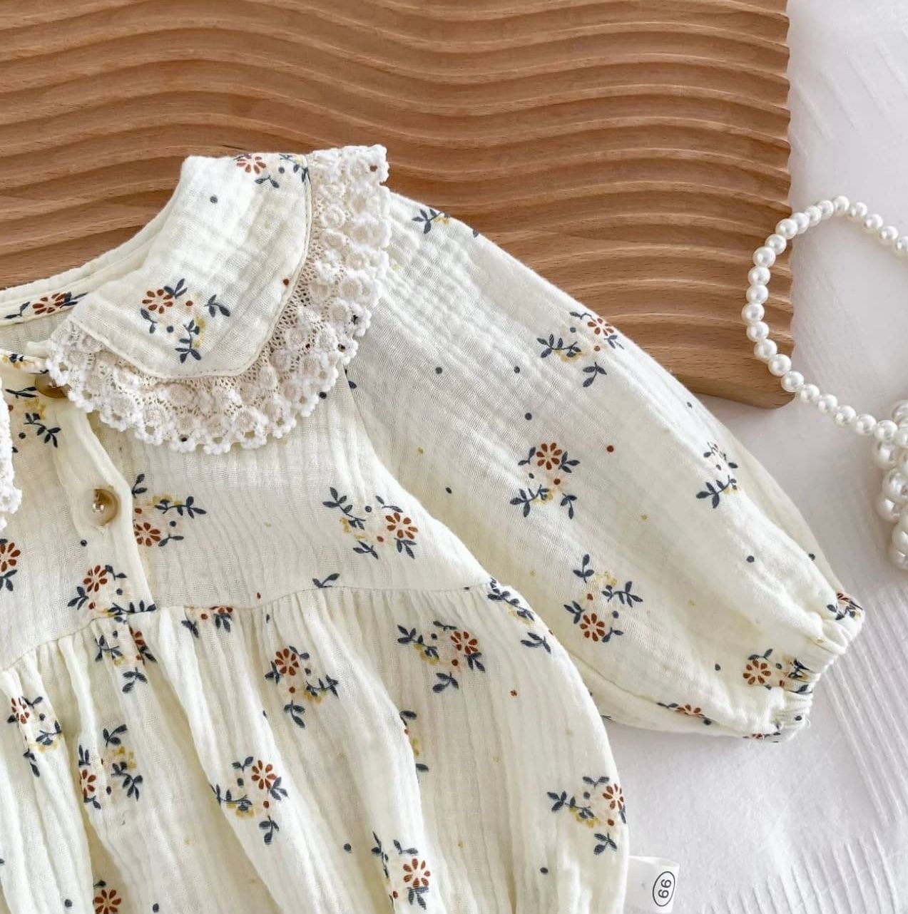 White cotton dress with delicate floral pattern and ruffled neckline laid flat on brown textured background.