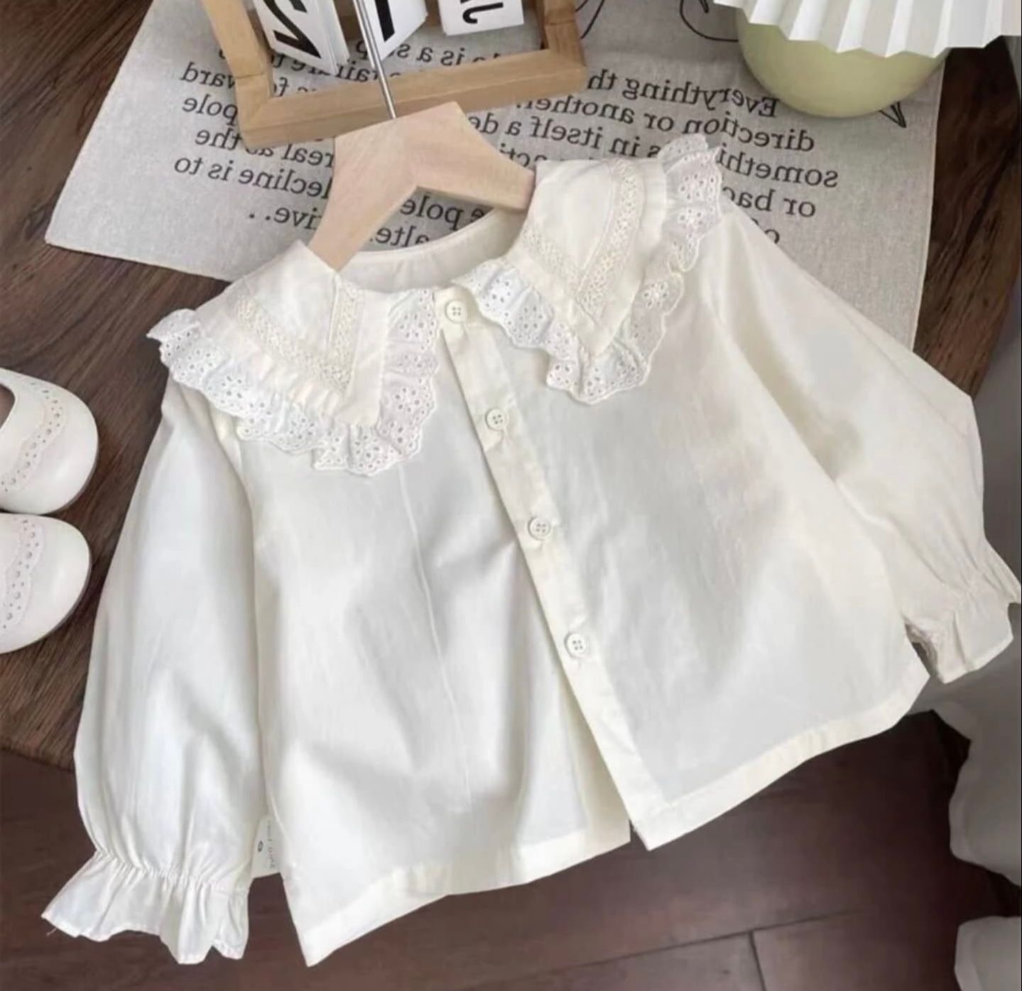 White romantic ruffle collar blouse with long sleeves and button front closure displayed on wooden hanger.