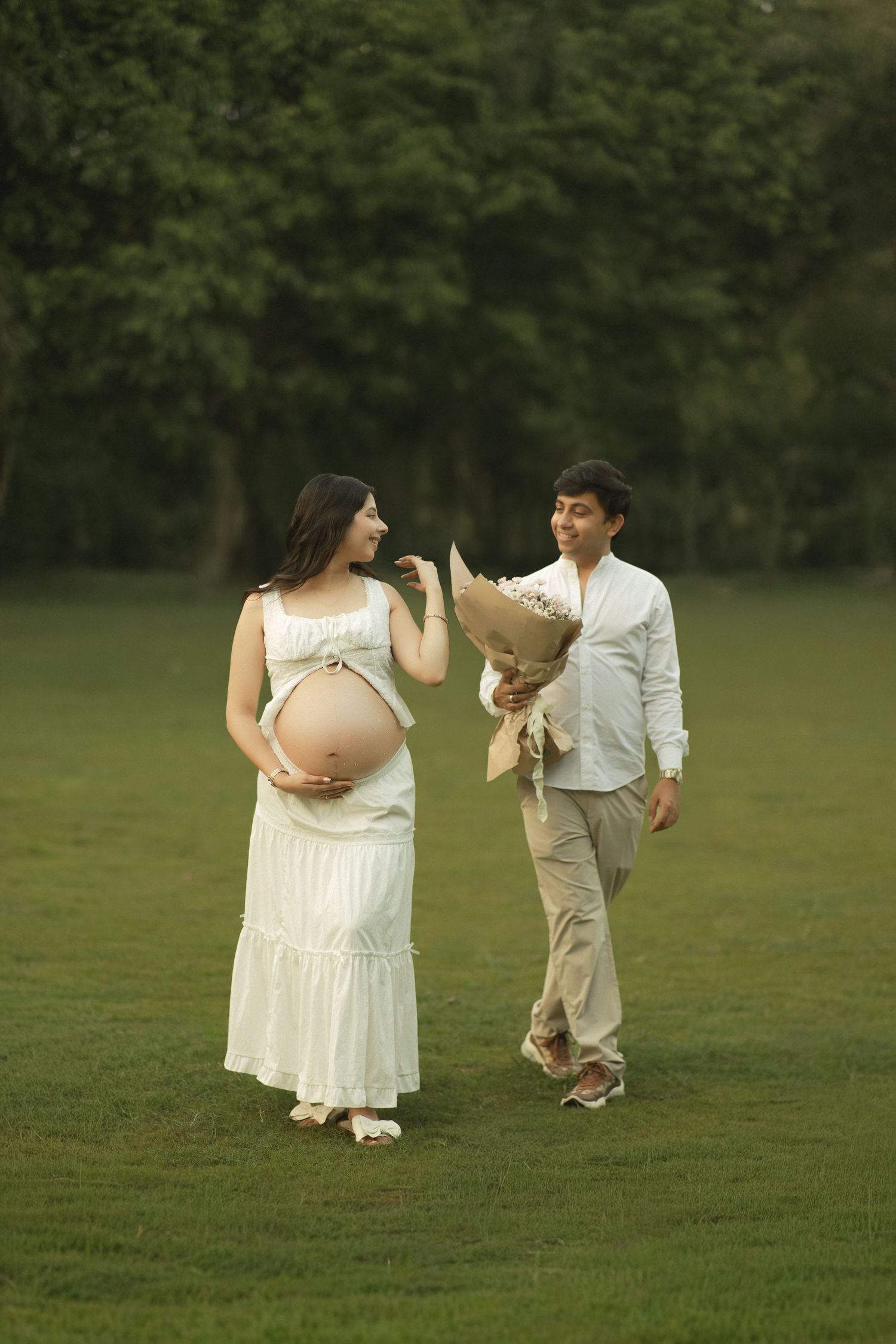A mother and child in white outfits dance together on a green lawn during a heartwarming outdoor photo session.