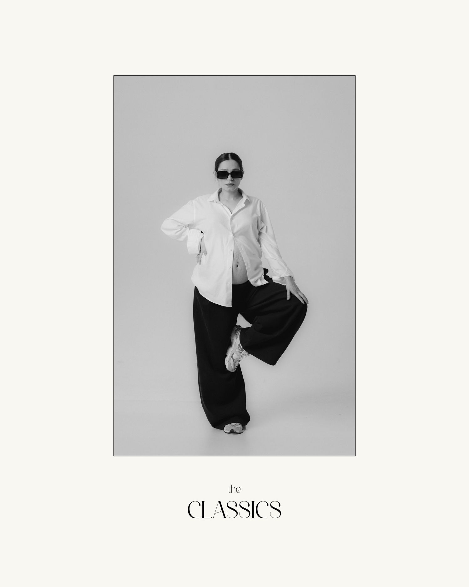 Woman posing in white oversized shirt and wide-leg black trousers with sunglasses for The Classics collection.