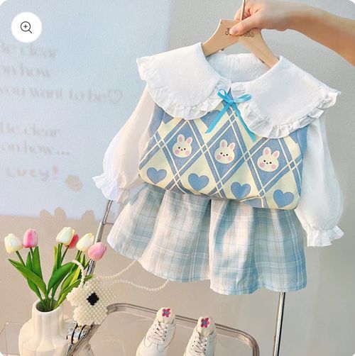 Baby outfit with blue bunny print vest, white ruffle collar blouse, and plaid shorts displayed with pink tulips.