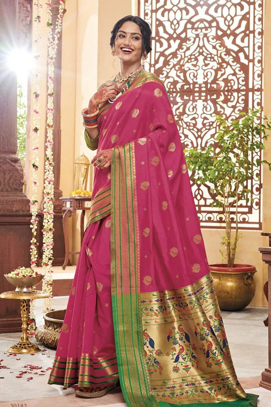 Pink and gold silk saree with intricate border design displayed in an ornate traditional setting.