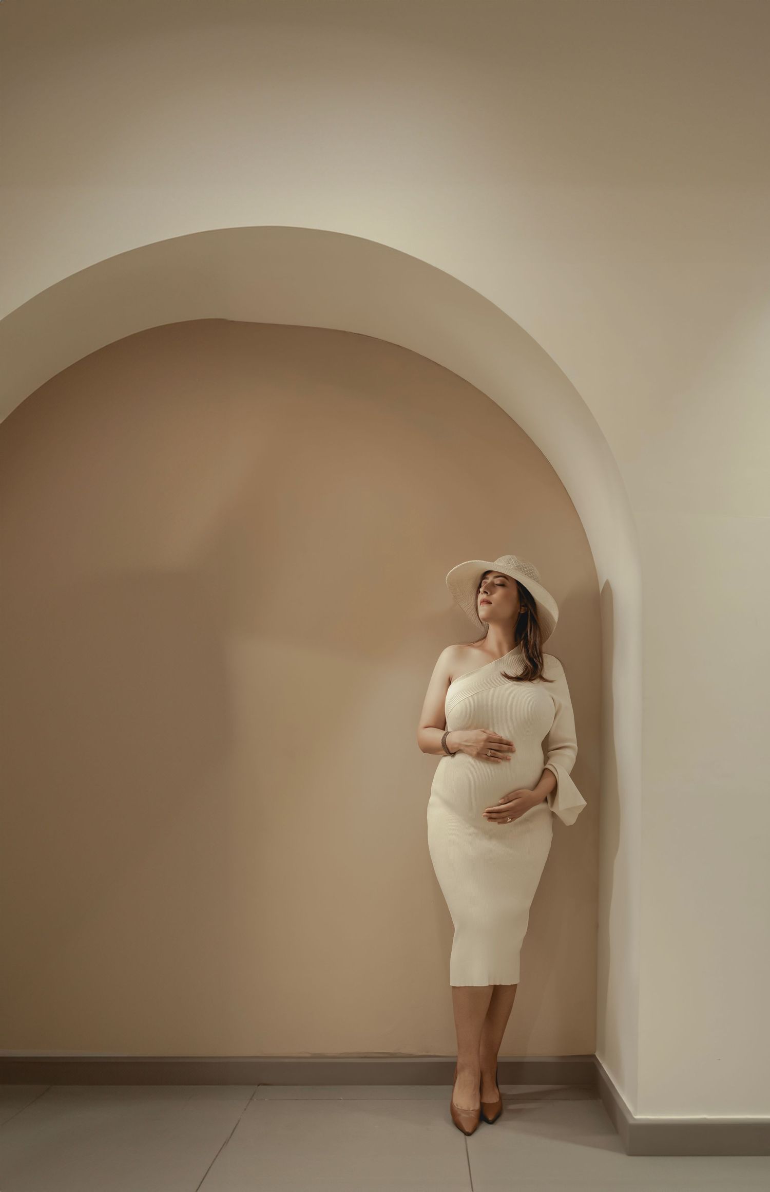 Artistic maternity portrait series in cream-colored fitted dress against neutral backdrop.