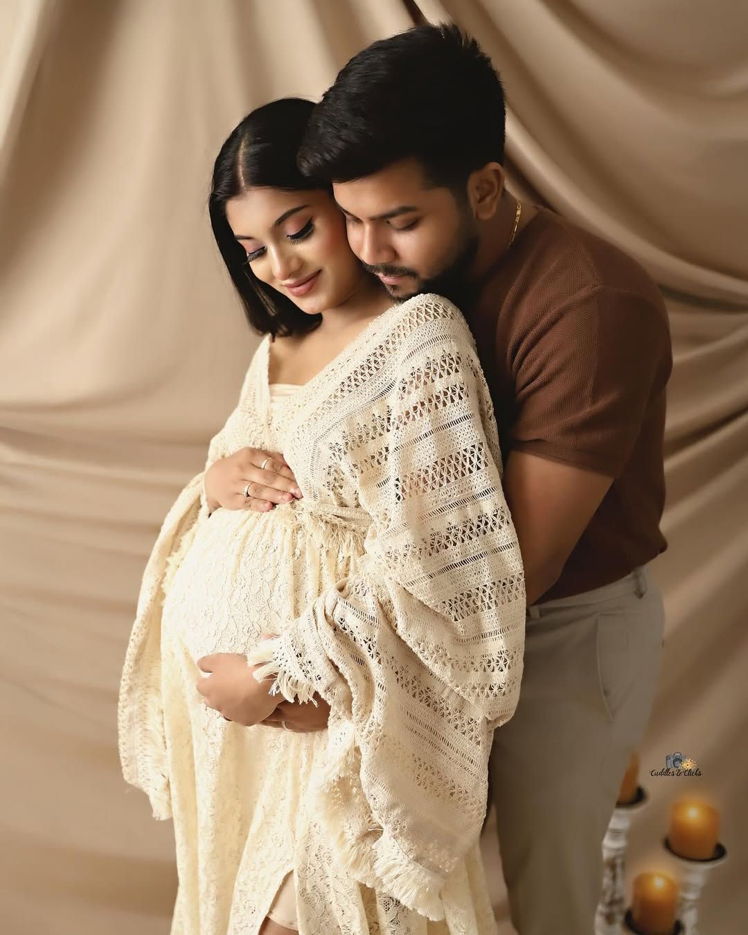 Tender maternity moment captured against cream backdrop with soft lighting.