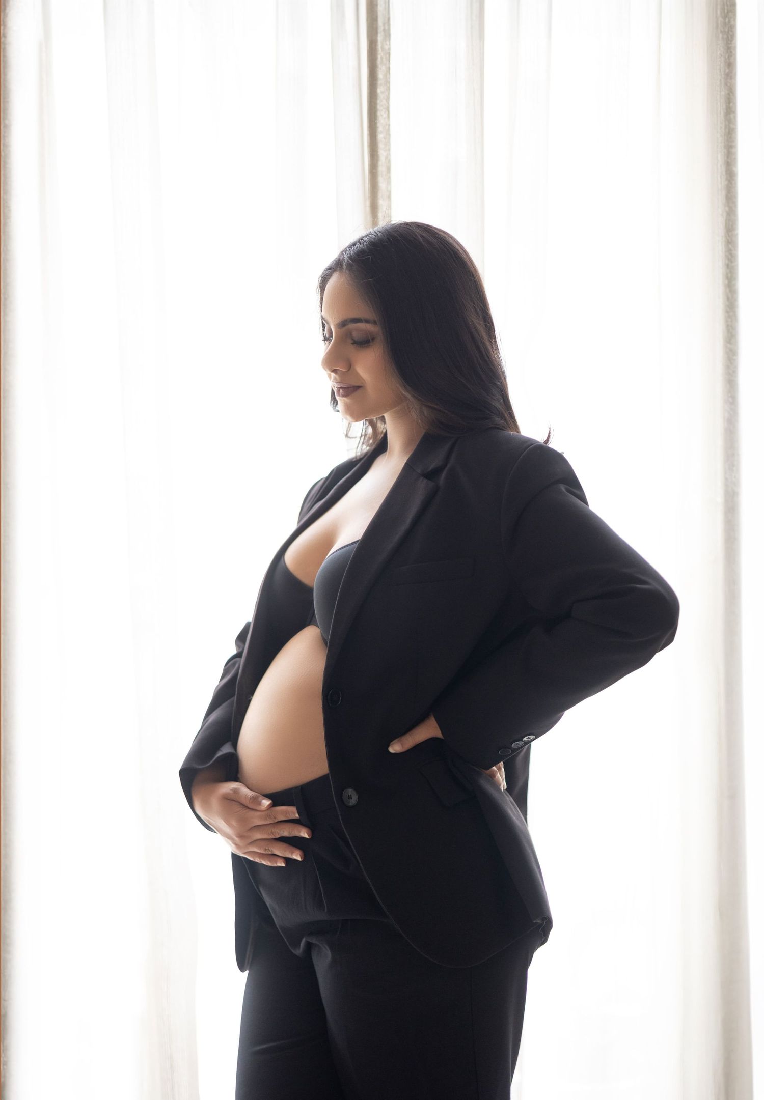 Artistic maternity photo shoot in black dress against white background showing silhouettes of pregnant woman.