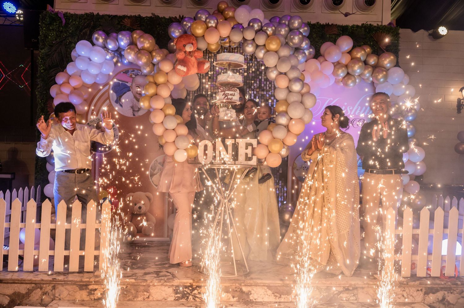 A balloon-decorated party venue with white picket fences and sparklers creating a magical celebration atmosphere.