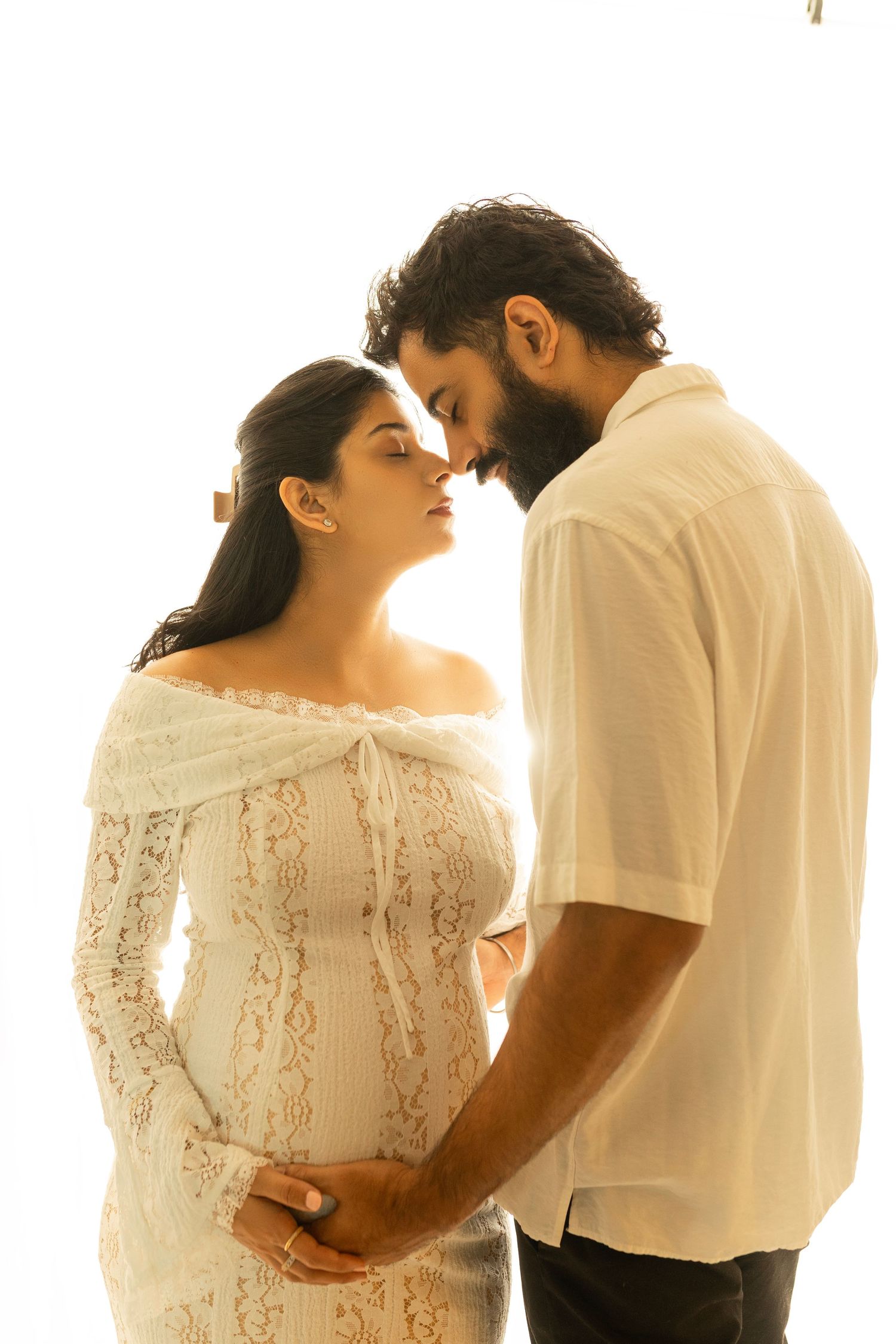 Intimate maternity portrait in white lace dress with romantic lighting.