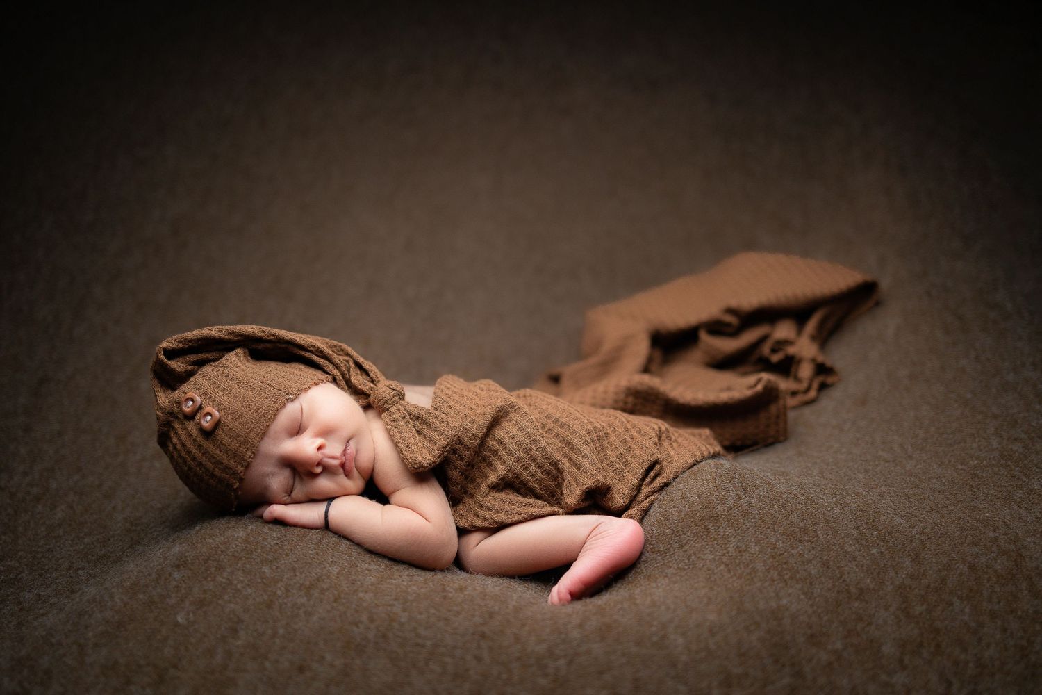 A tender newborn photography composition showing a sleeping baby in sepia tones with blurred background lighting.
