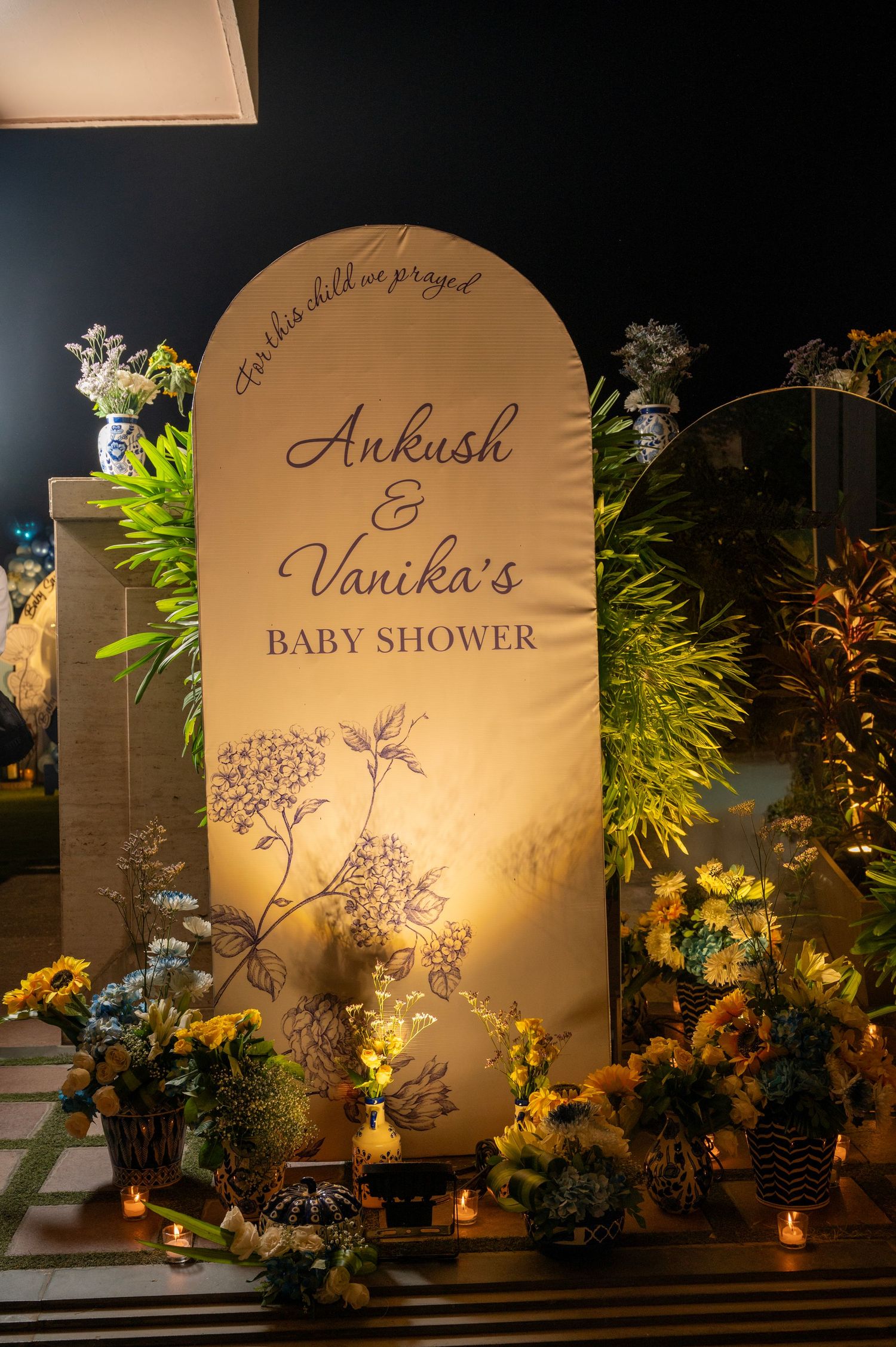 Illuminated wedding backdrop with elegant floral designs and custom text displays at night with warm lighting.