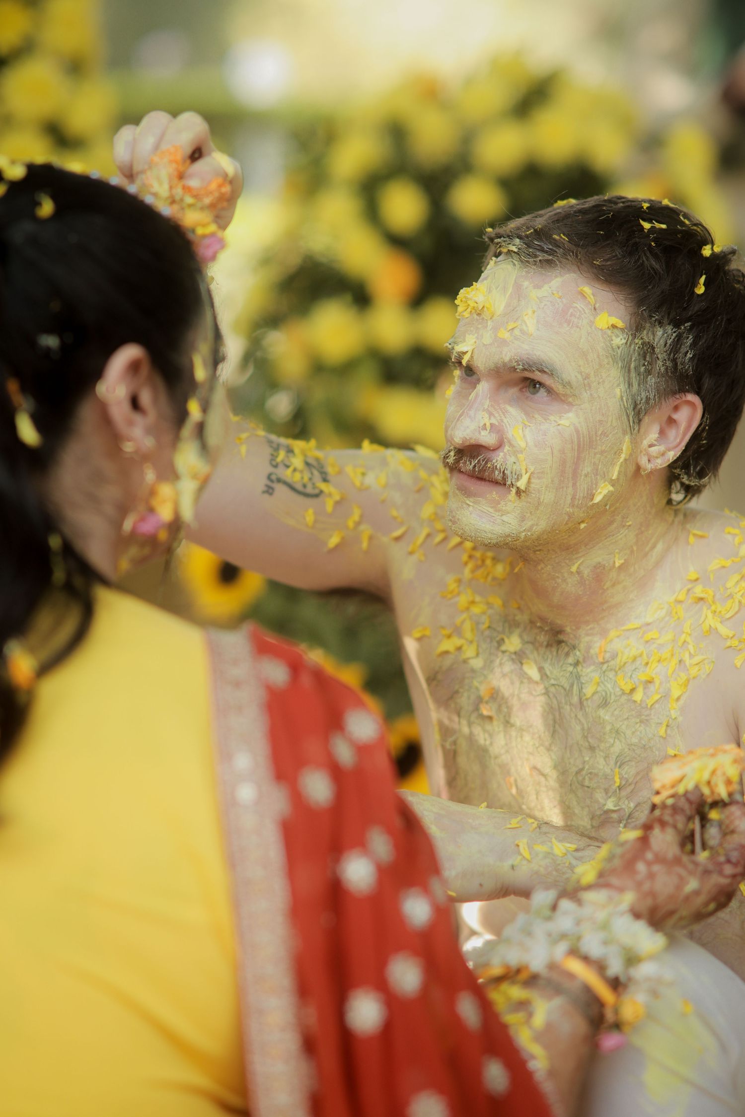 Couple celebrating Haldi ceremony with yellow turmeric paste and marigold flowers during Indian wedding ritual.