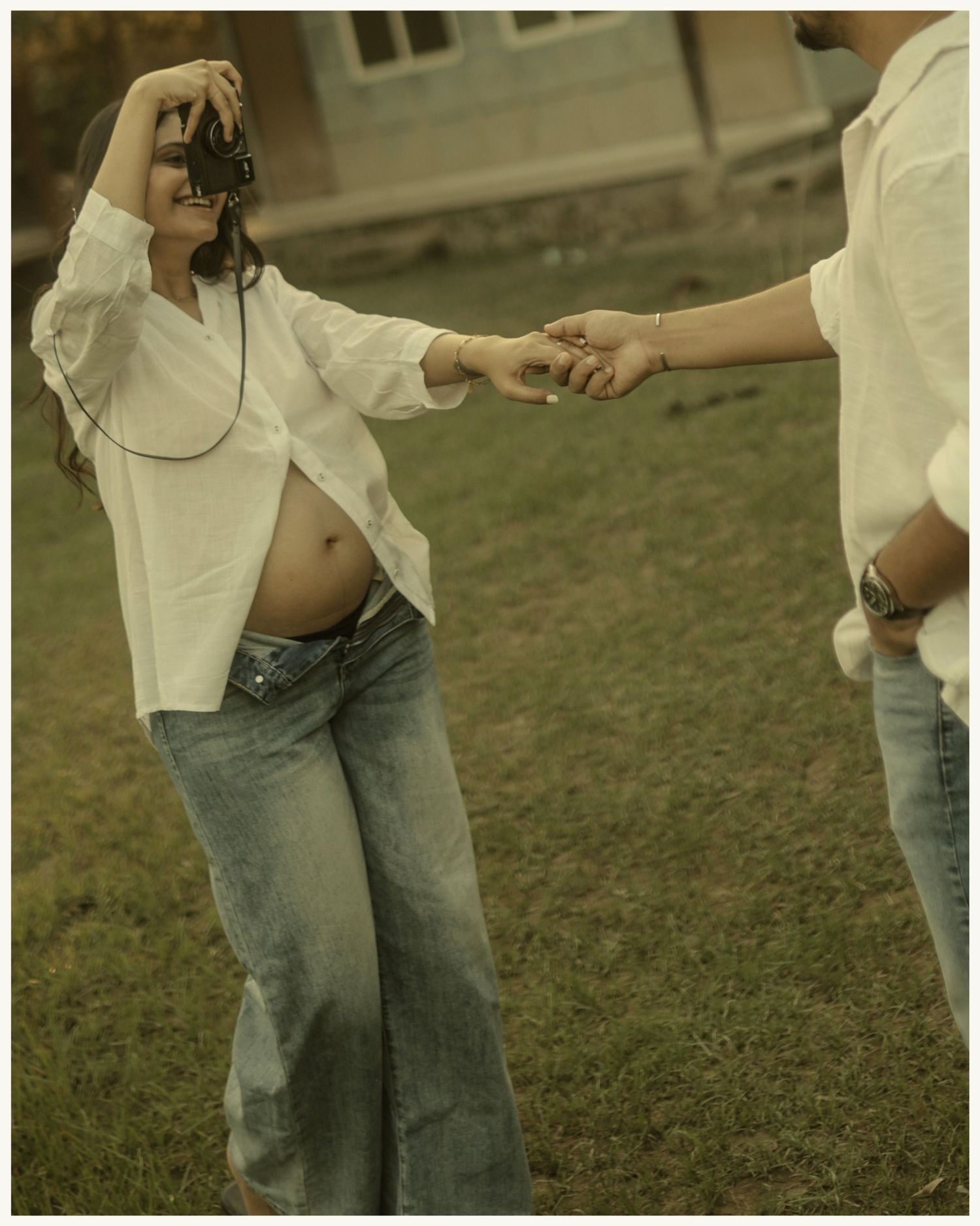 Pregnant woman in white shirt and jeans holds hands with partner outdoors during a maternity photo shoot.