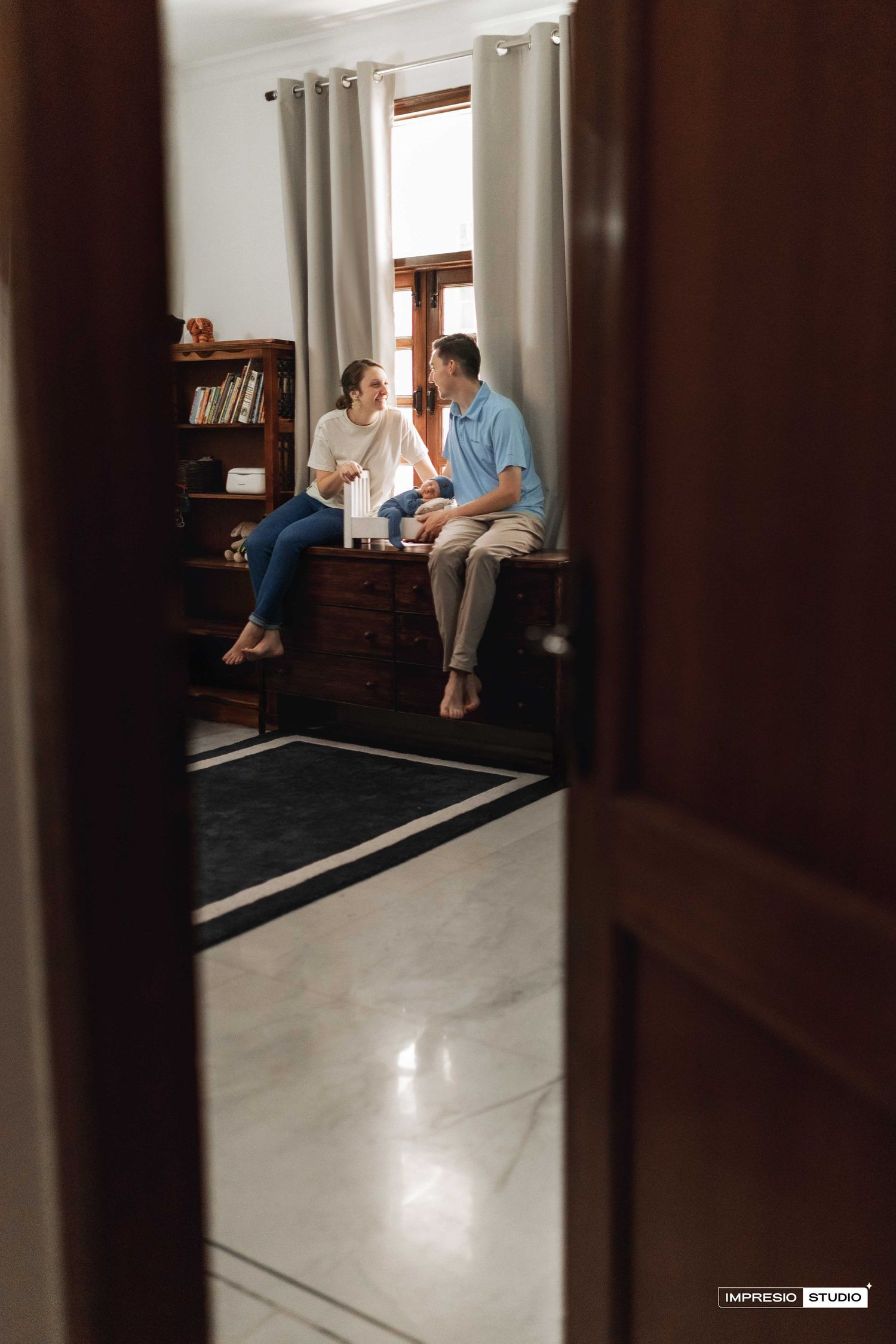 Couple sitting on wooden dresser by window having a conversation in a classic home interior.