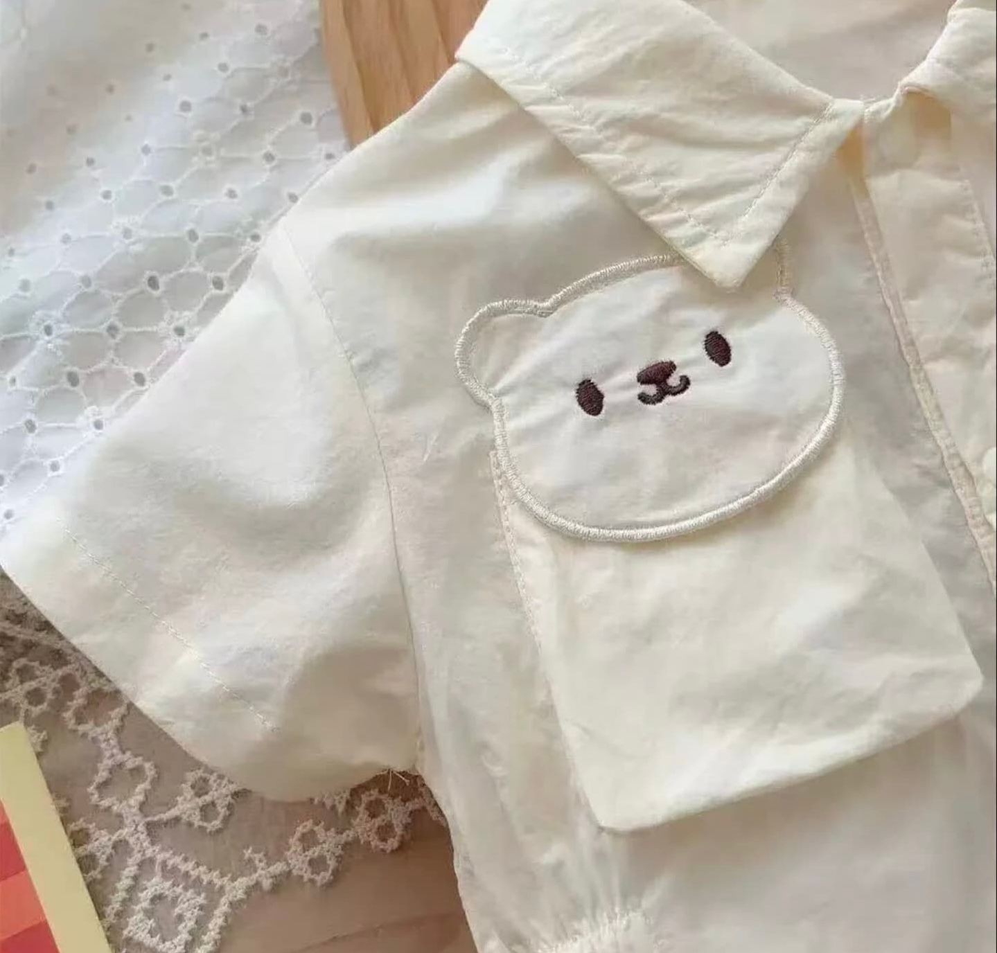 White garment pocket features an adorable embroidered polar bear or seal face design with simple black dot eyes.