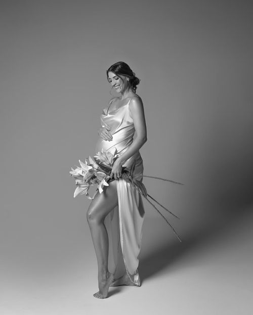 Artistic black and white maternity photoshoot sequence showing woman in flowing white dress holding calla lilies.