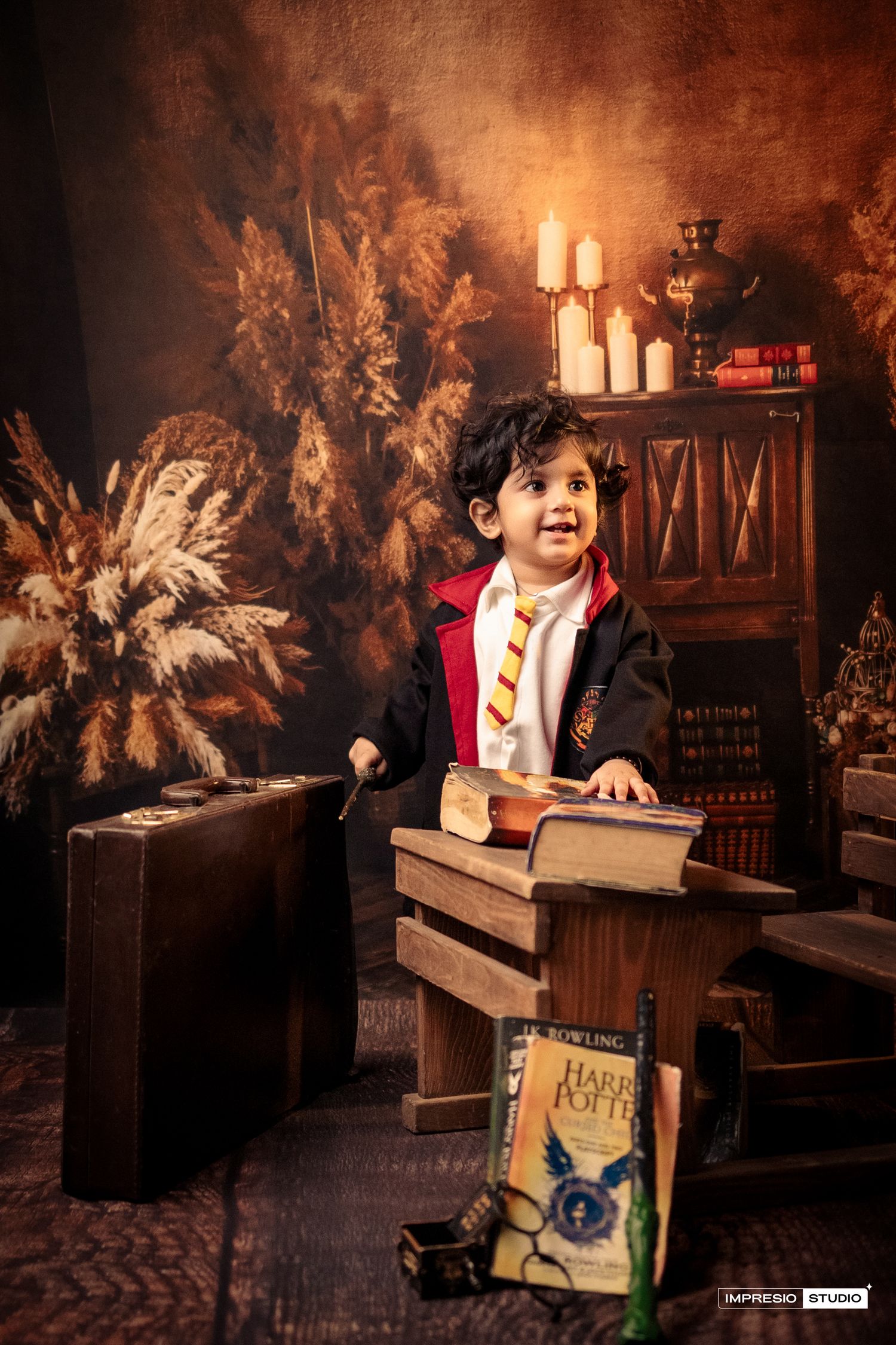 A magical Harry Potter themed photo setup with books, candles, and pampas grass decorations in warm brown tones.