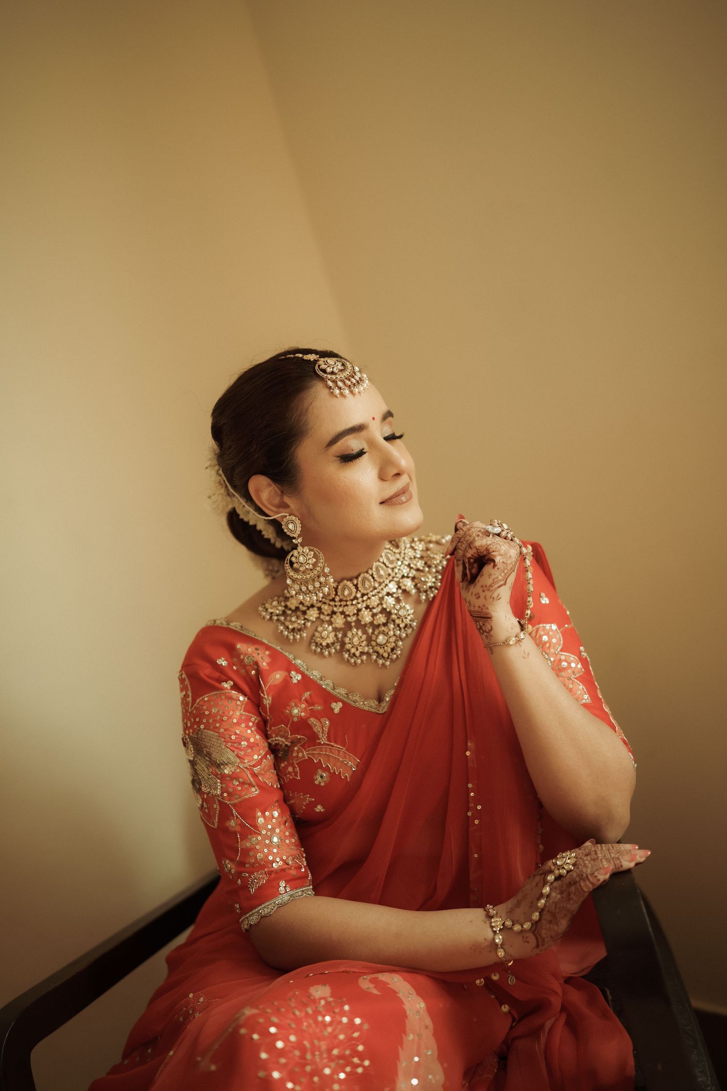 Bride in red saree with gold kundan jewelry poses gracefully during bridal preparation.
