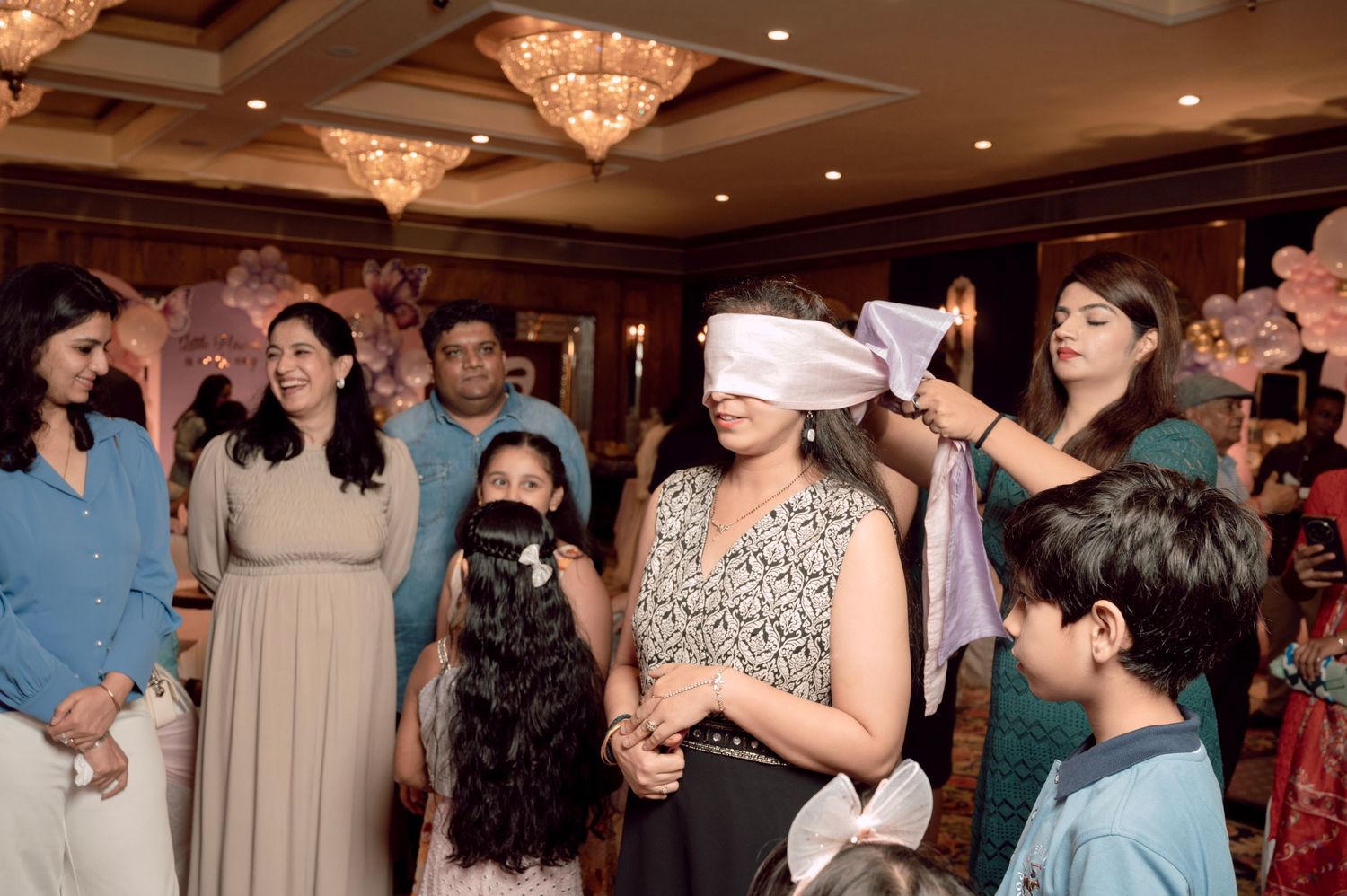 Group of people at a party playing a blindfold game in a decorated banquet hall.
