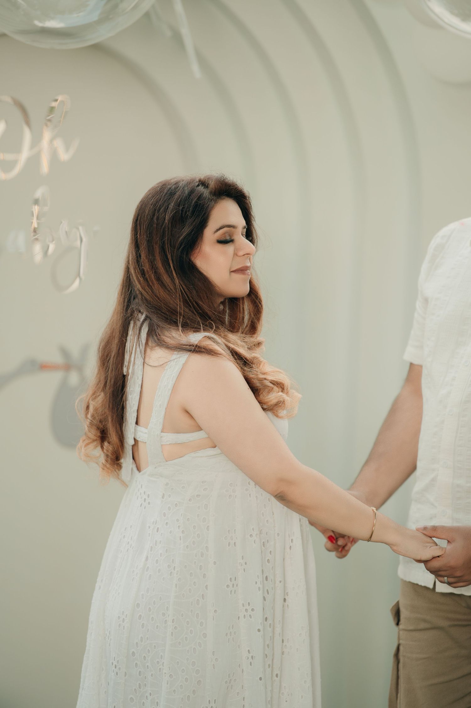 A woman in a white eyelet dress holds hands with a partner at an elegant baby shower celebration.
