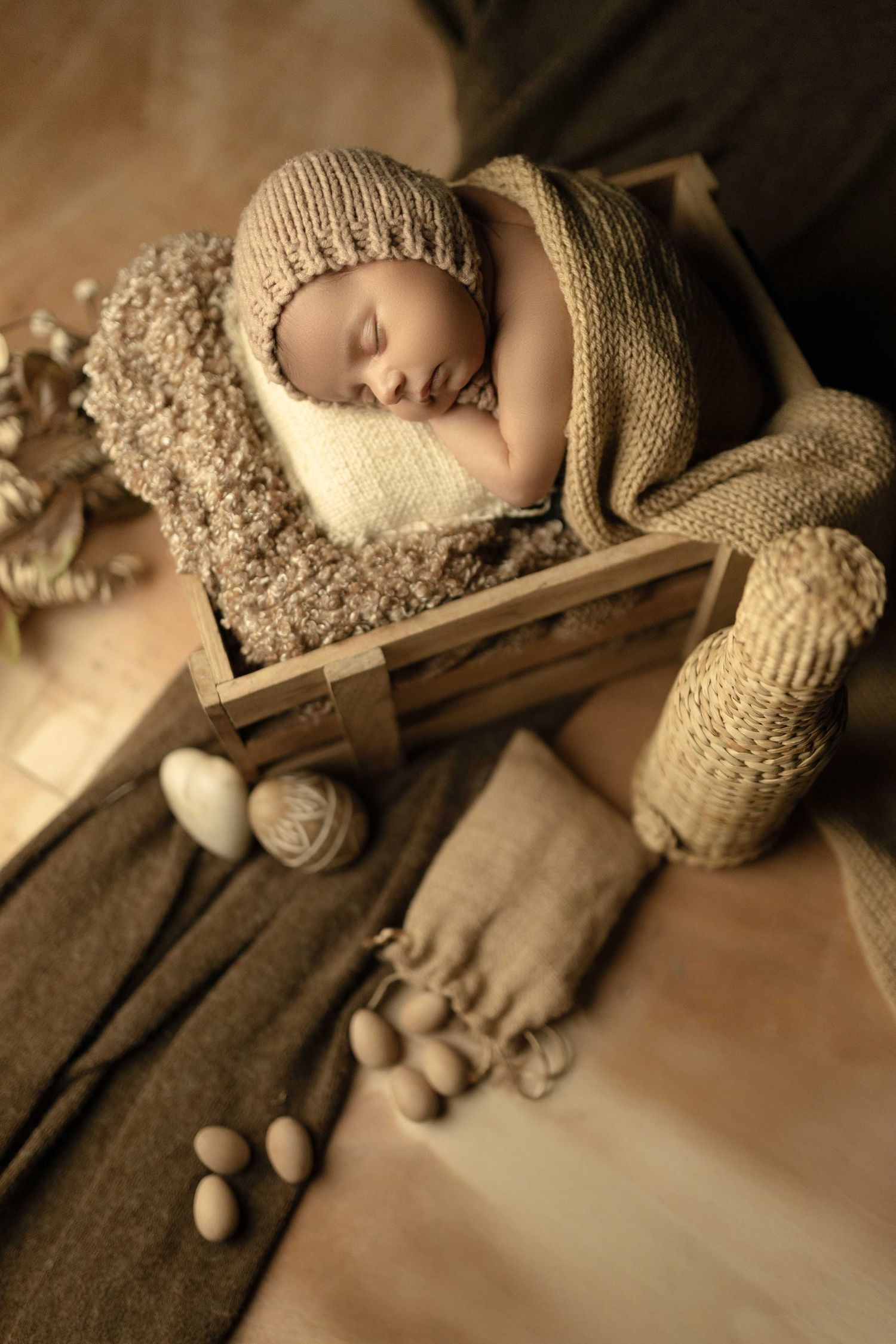 Sleeping newborn baby in knit hat posed in rustic wooden crate with burlap and yarn props in warm neutral tones.
