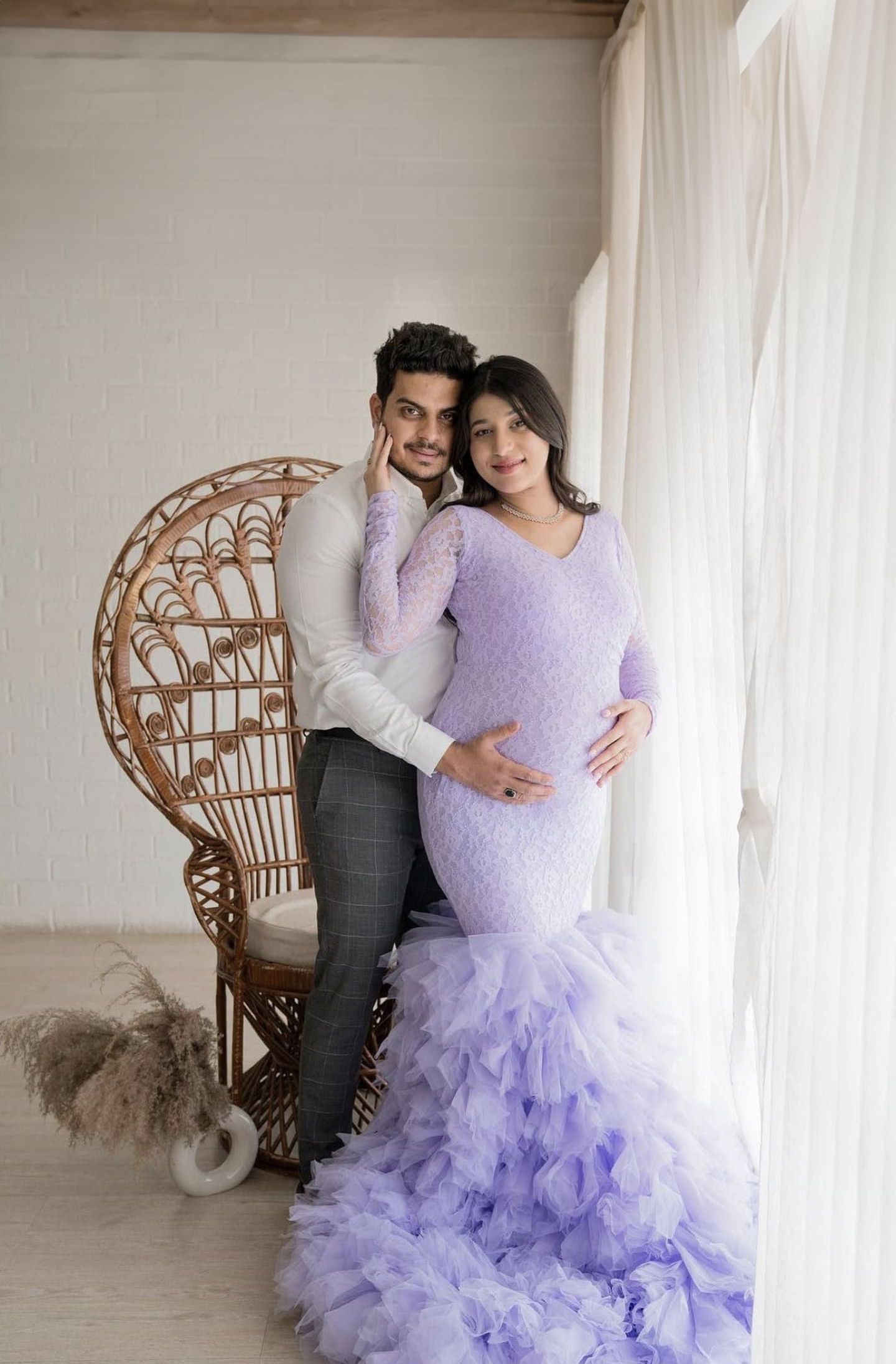 Romantic maternity portrait with couple by wicker peacock chair in lavender ruffled gown.