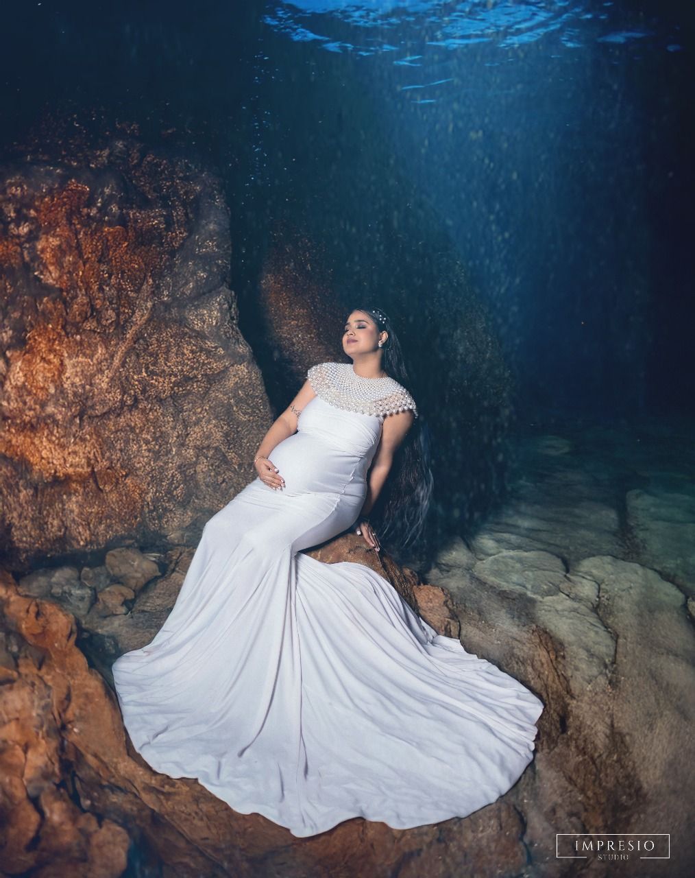 Ethereal underwater maternity portrait with flowing white dress in crystal clear cave waters.