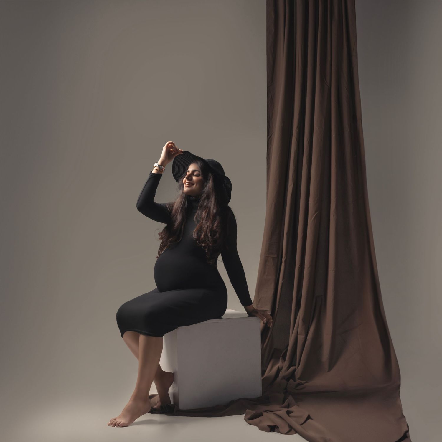 Elegant maternity portrait with brown drapes and dramatic lighting in studio setting.