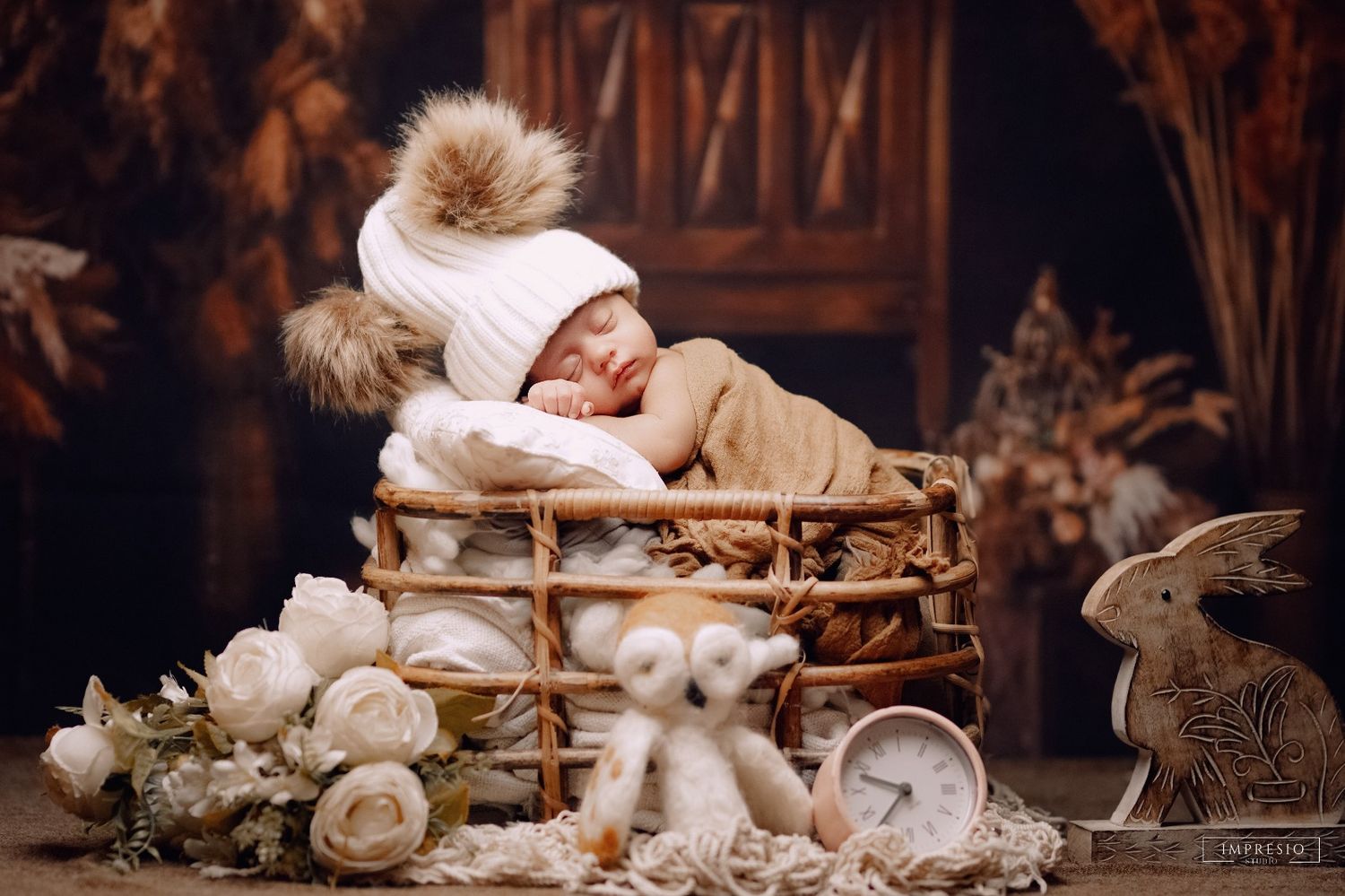 Baby resting in rustic basket surrounded by teddy bears and vintage decor for newborn photograph.