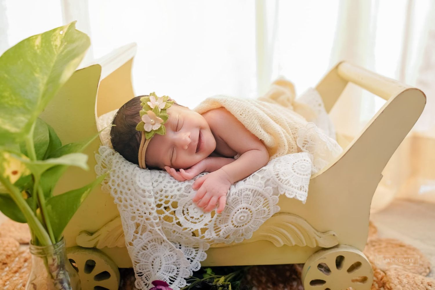 Newborn baby sleeping peacefully in a small decorative wooden bed, wrapped in lace, wearing a floral headband.