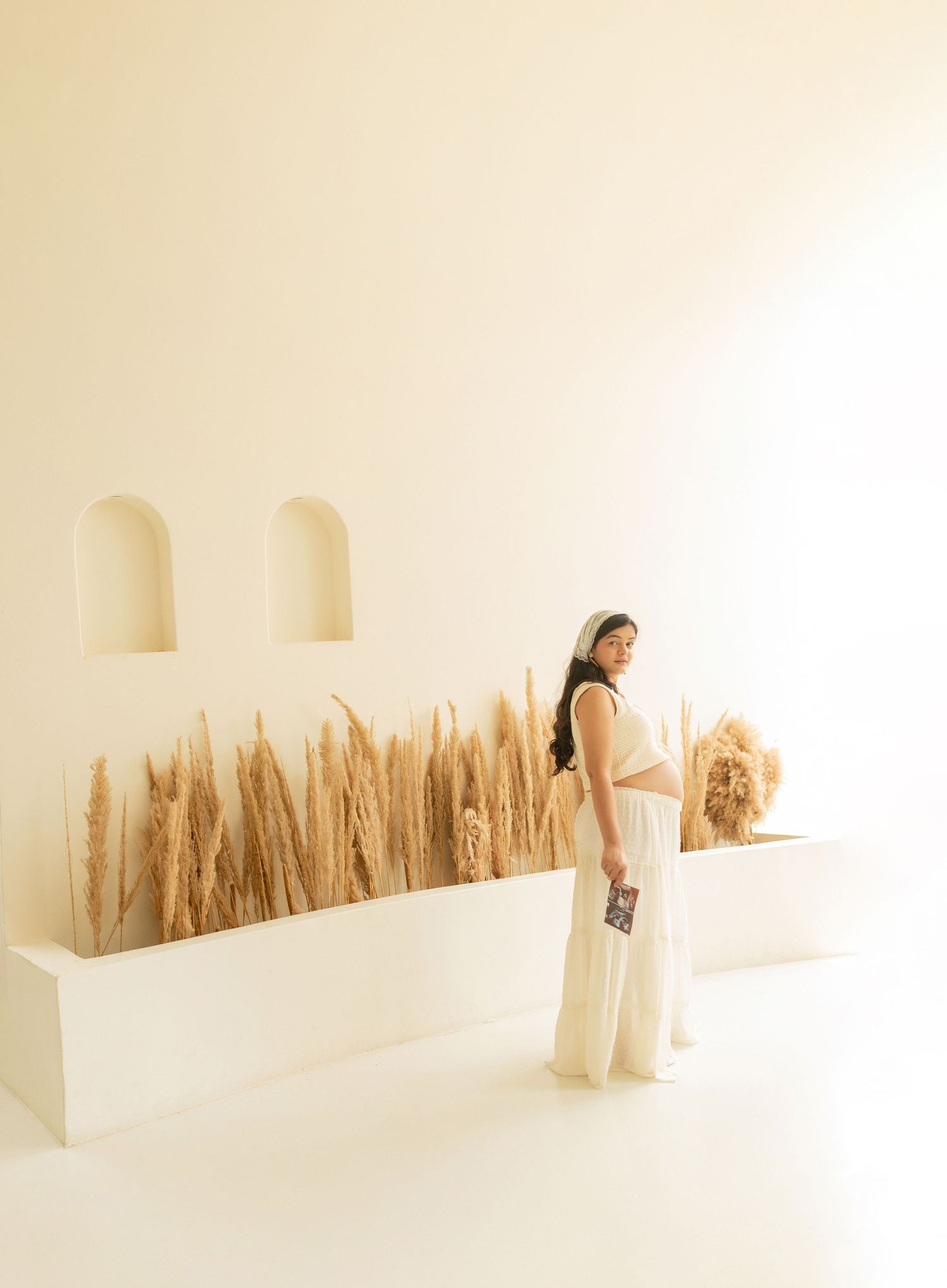 A minimalist white interior space features dried pampas grass arranged along a wall, creating an organic textural display.