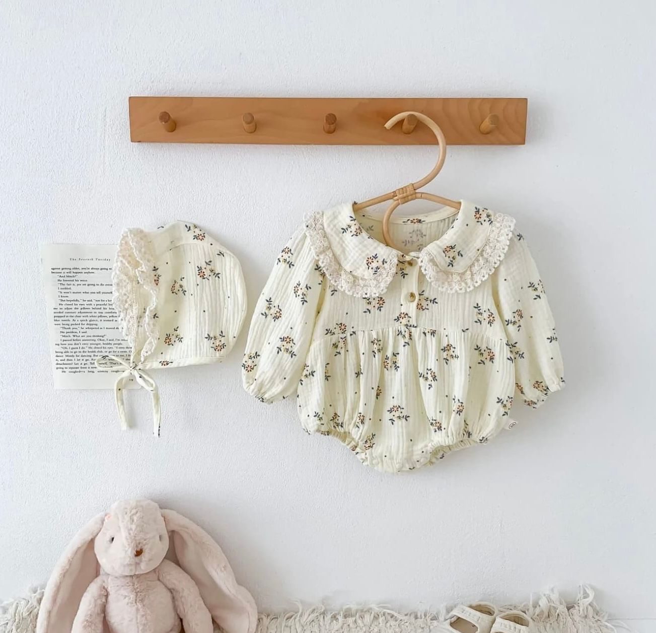 White floral smocked dress with puff sleeves and vintage style hangs on wooden wall hook next to plush bunny toy.