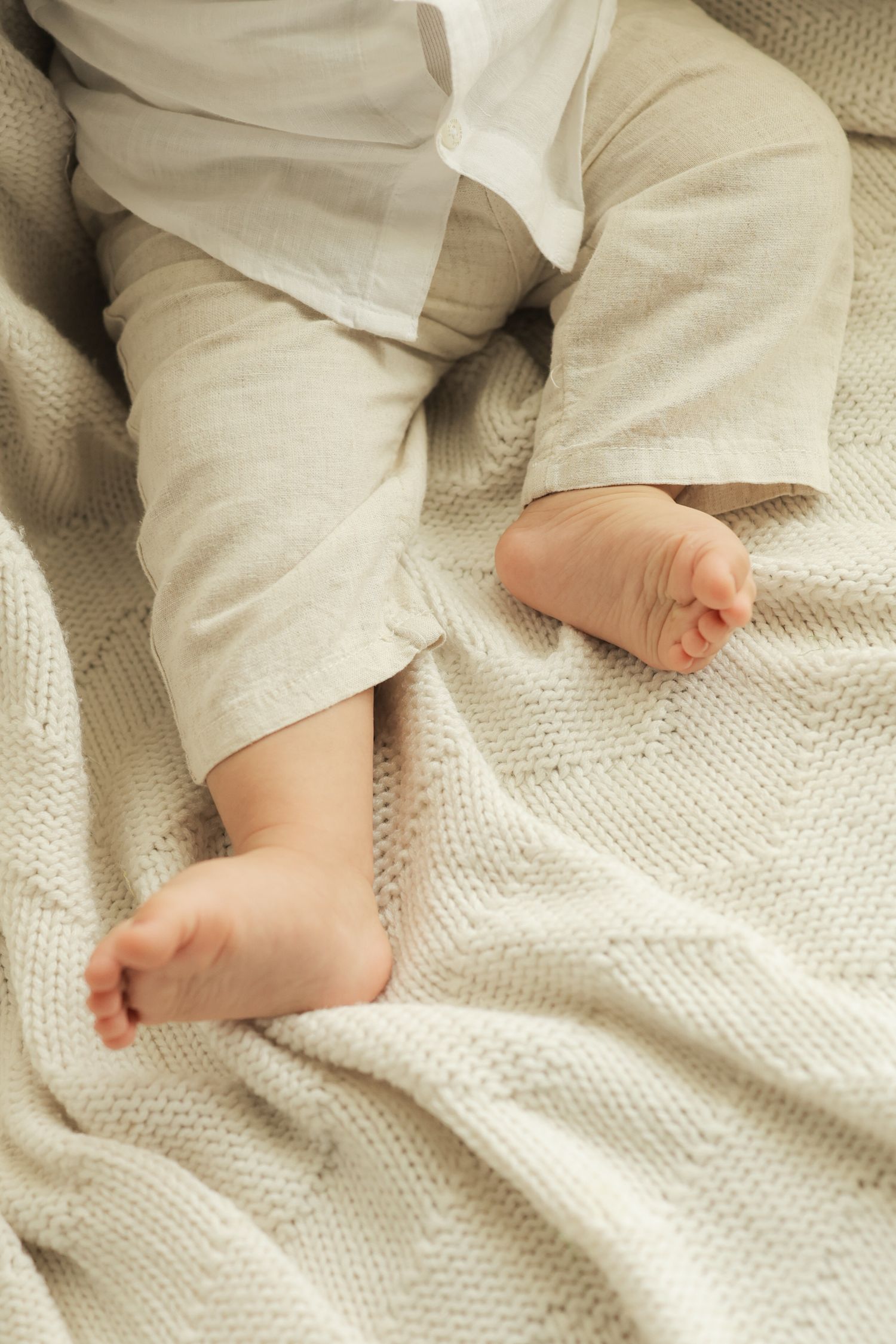 Close-up of tiny baby feet resting on a soft cream knit blanket, with infant wearing beige pants.