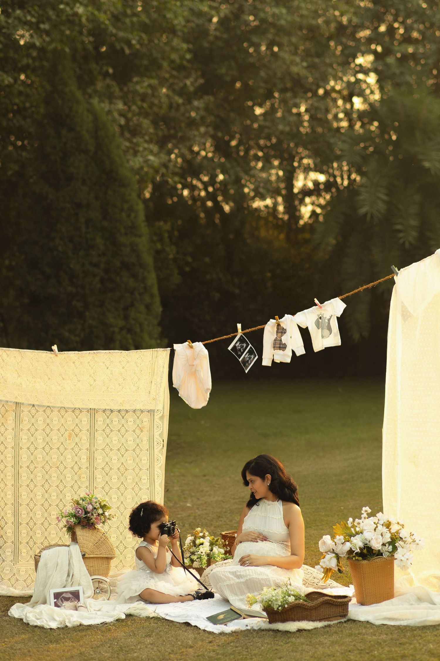 A vintage-inspired outdoor scene with white lace curtains hanging on clotheslines and floral arrangements at sunset.