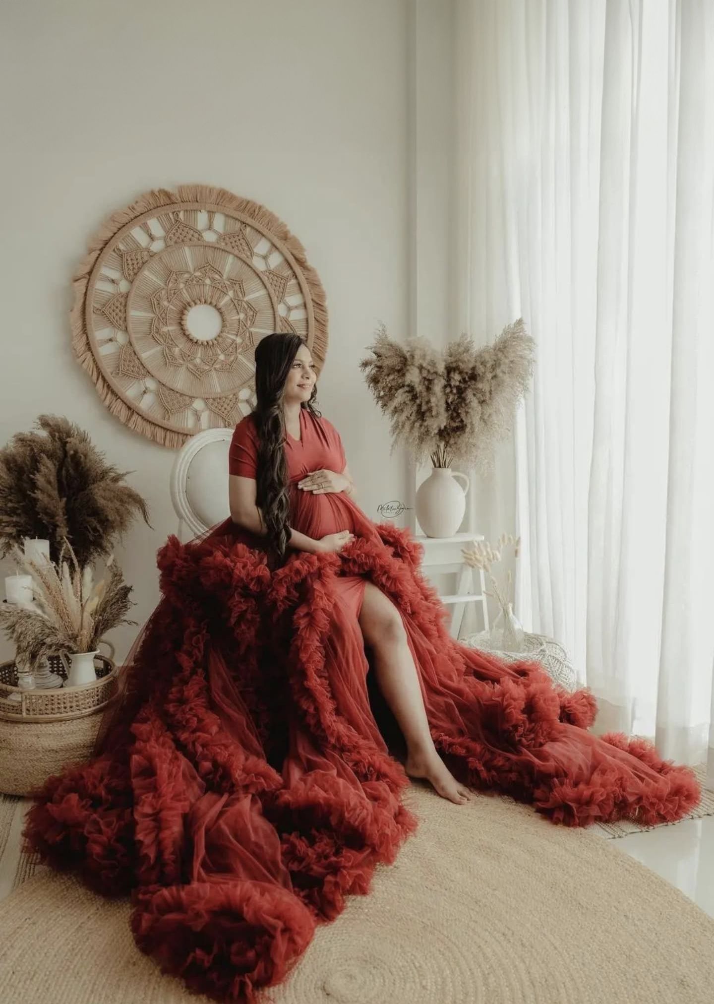 Maternity photo with flowing red dress against circular wall art and pampas grass decor.
