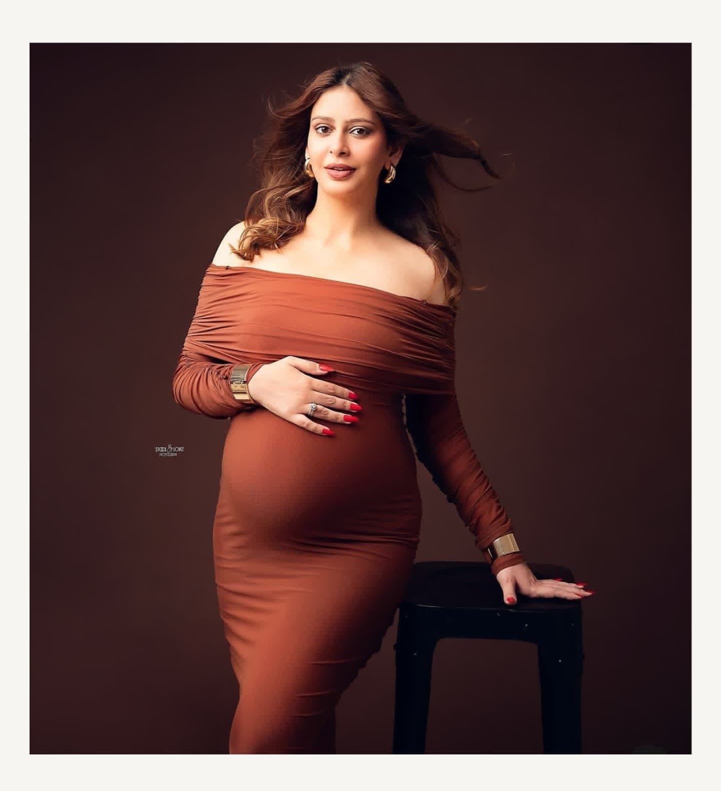 Dramatic maternity portraits in fitted rust dress with studio lighting.