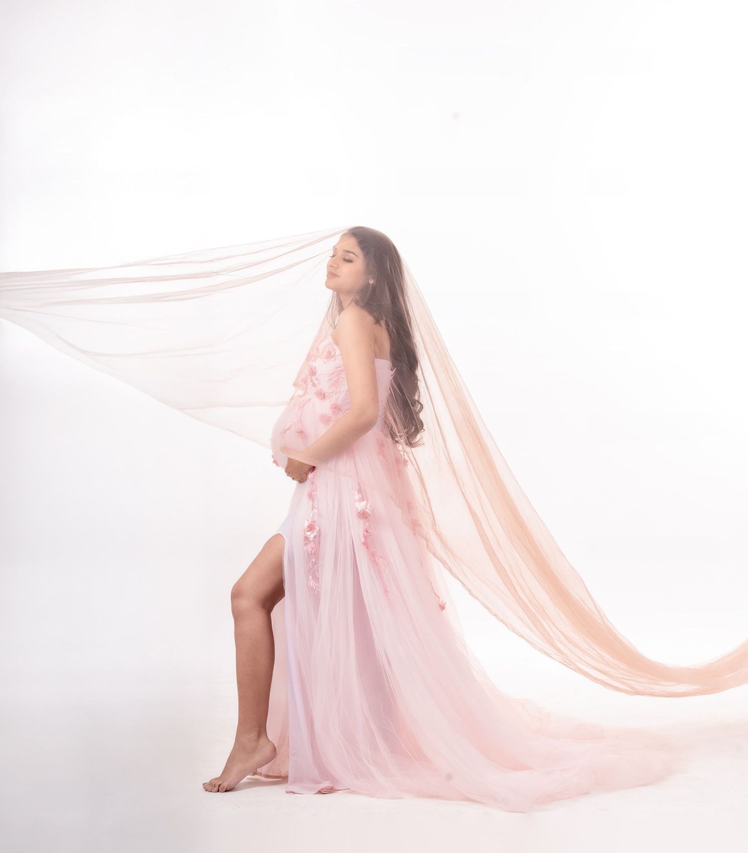 Artistic maternity photo series featuring flowing pink fabric against white background.