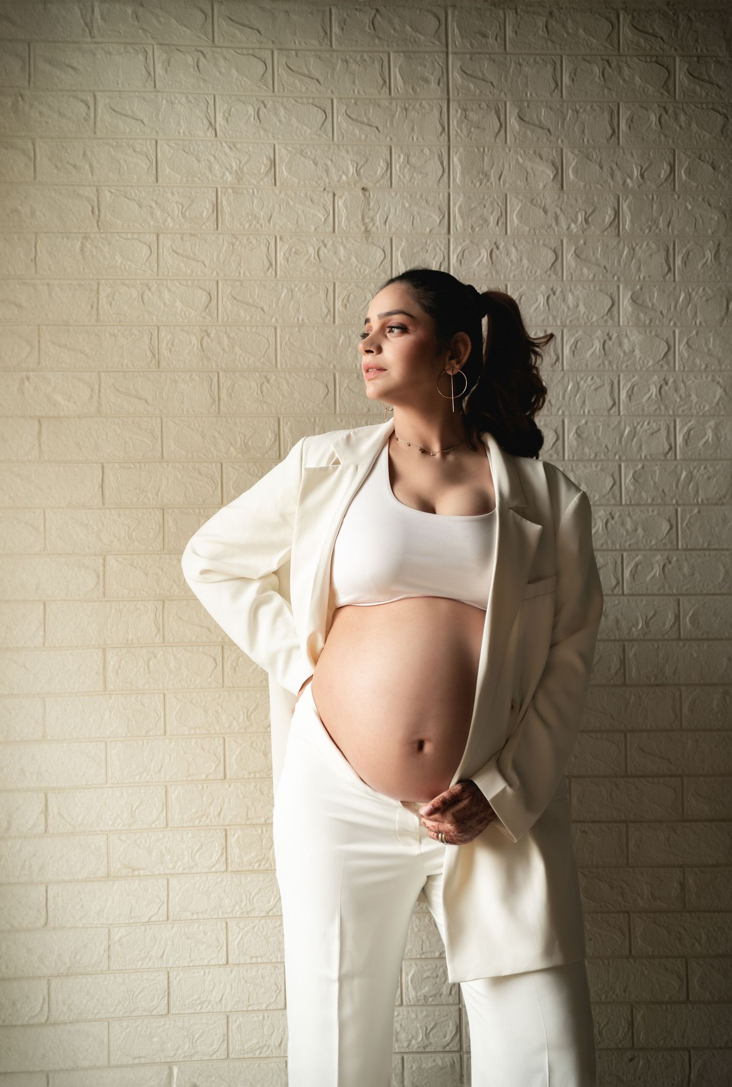 Maternity photography series showing pregnant woman in white outfit against brick wall.