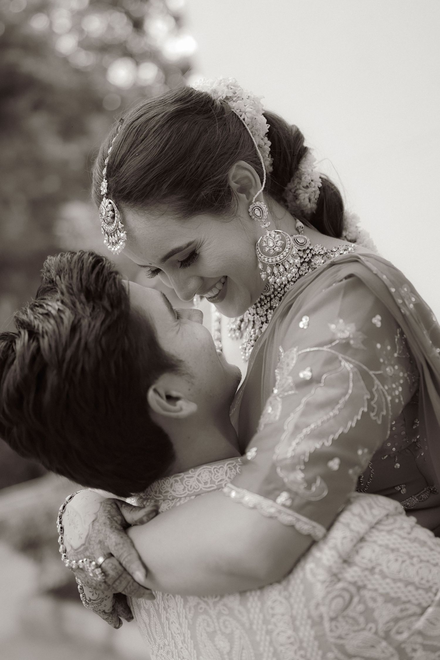 Black and white photo of an Indian bride and groom sharing a romantic moment, bride adorned in traditional jewelry.