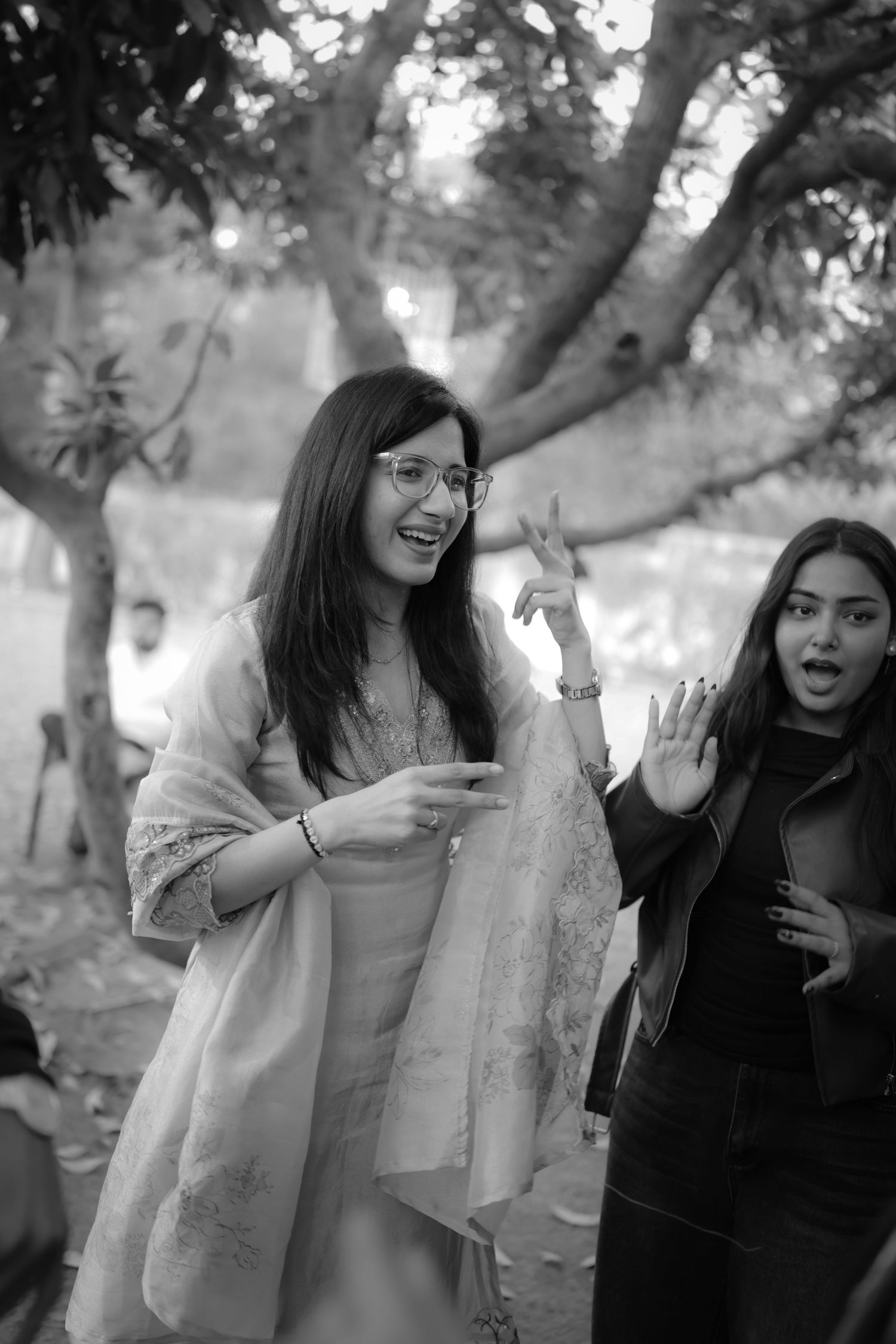 Two young women laughing and gesturing outdoors in black and white photo, trees in background.