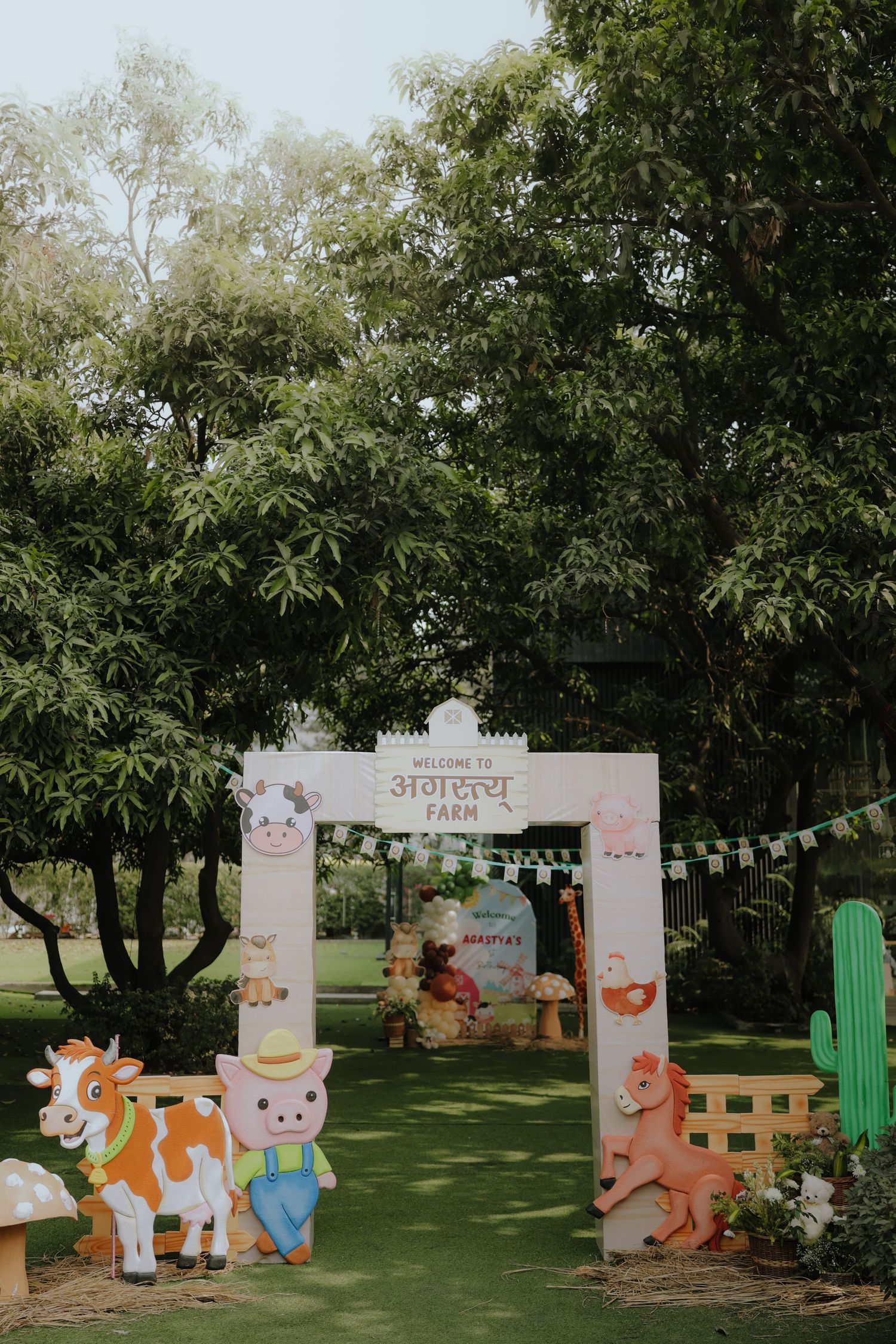 Farm-themed birthday party entrance arch with cute animal cutouts, bunting, and welcome sign in an outdoor garden setting.