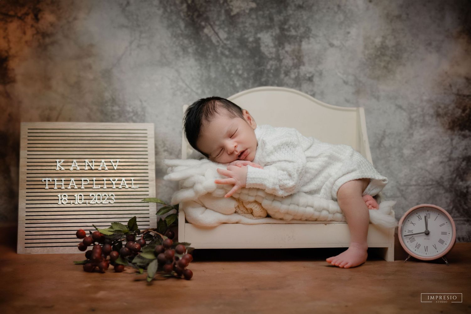 Newborn baby Kanav Thapliyal sleeping peacefully on a miniature bed with a clock and letter board in a studio photo.