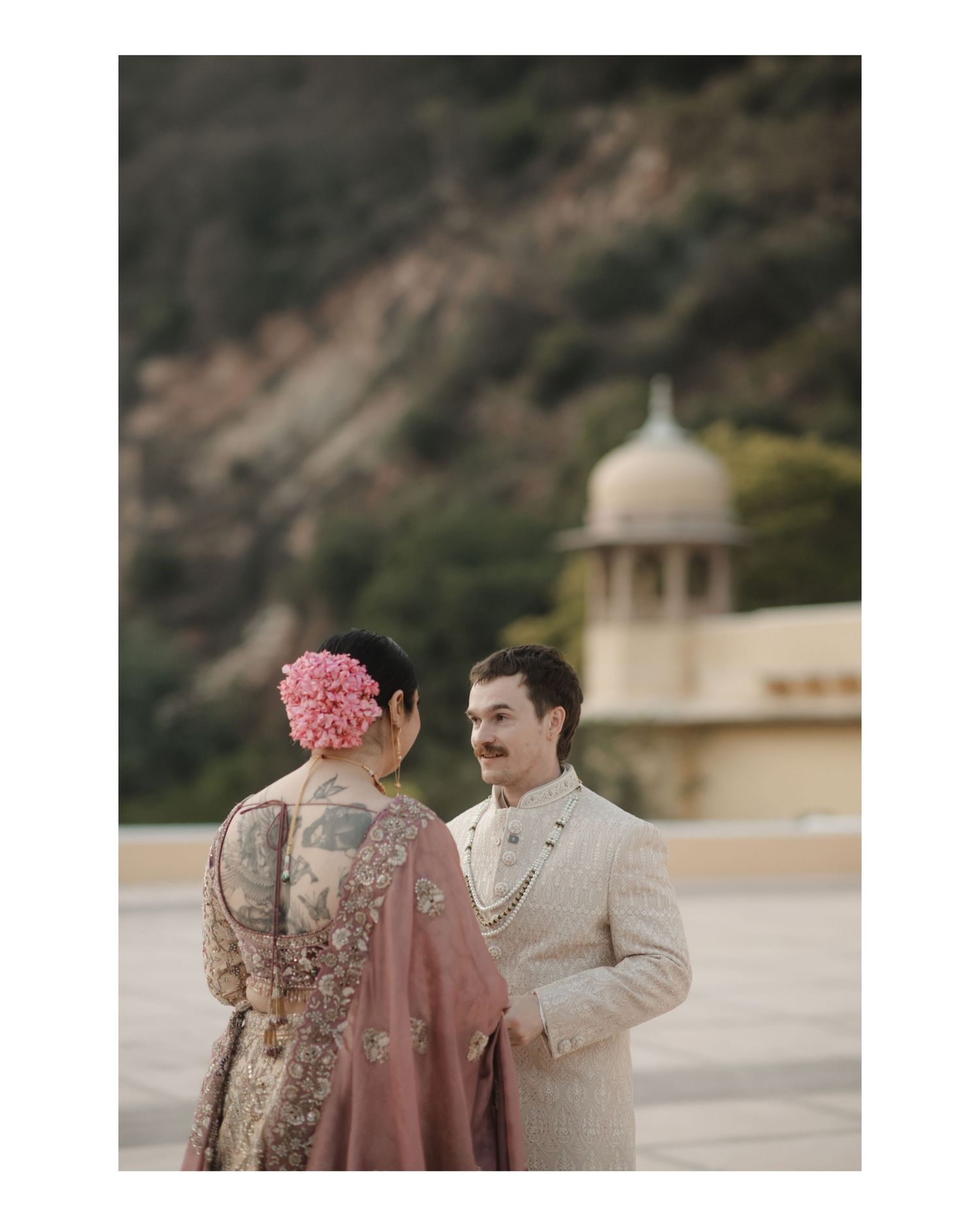 A couple in traditional wedding attire sharing an intimate moment at a grand outdoor venue.