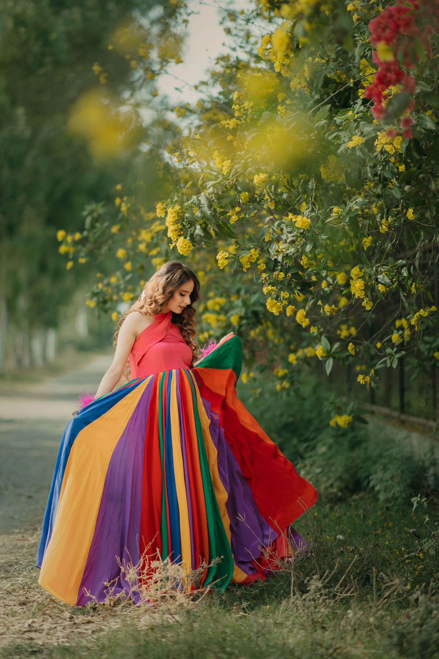 Rainbow colored flowing dresses create a vibrant maternity pose against lush greenery and yellow flowers in outdoor portraits.