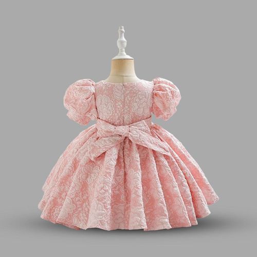 Pink floral lace baby girl's formal dress with puff sleeves and bow detail displayed on beige mannequin.