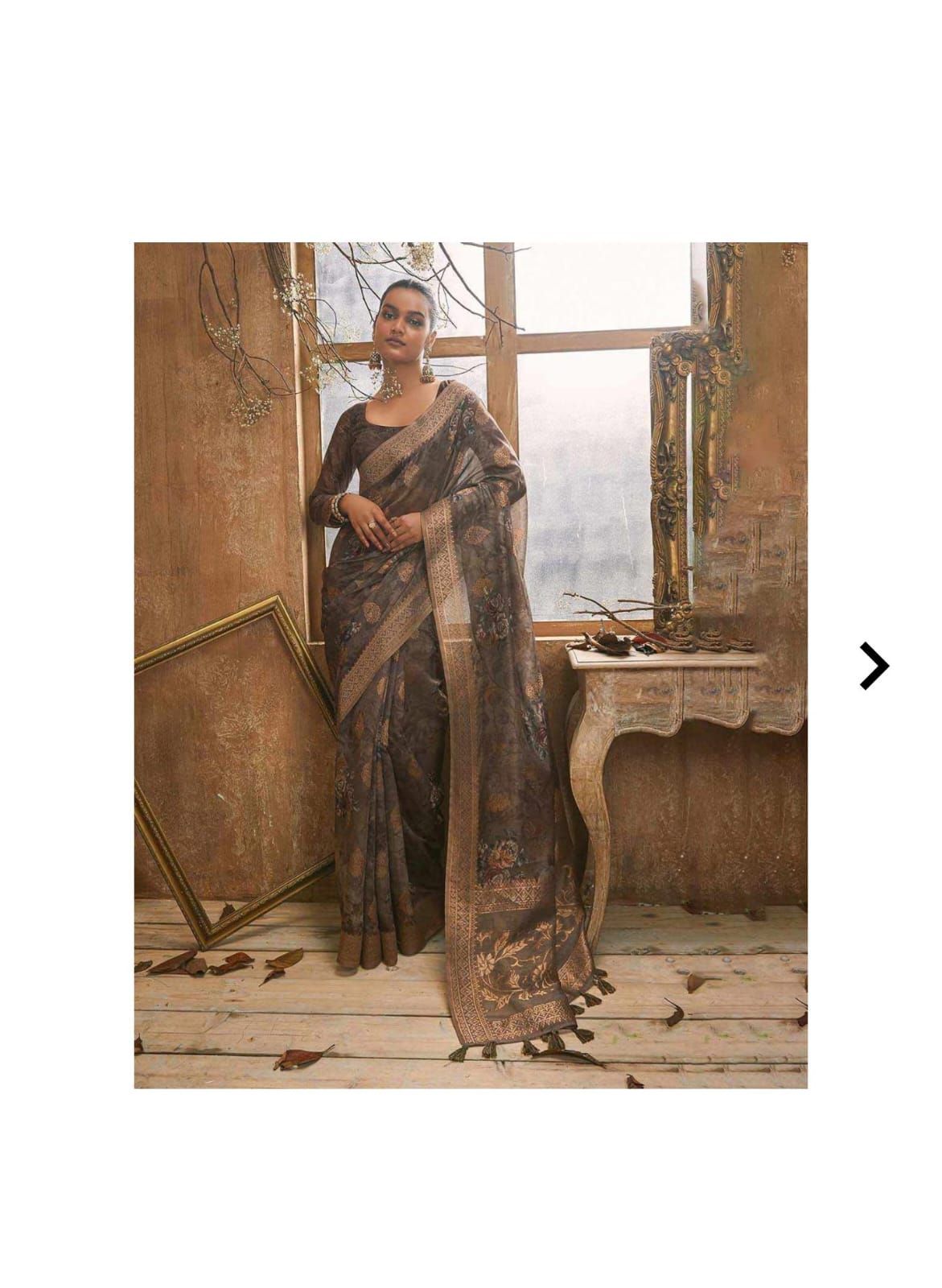 Elegant gray organza saree with delicate floral patterns and tassels displayed near a rustic window.