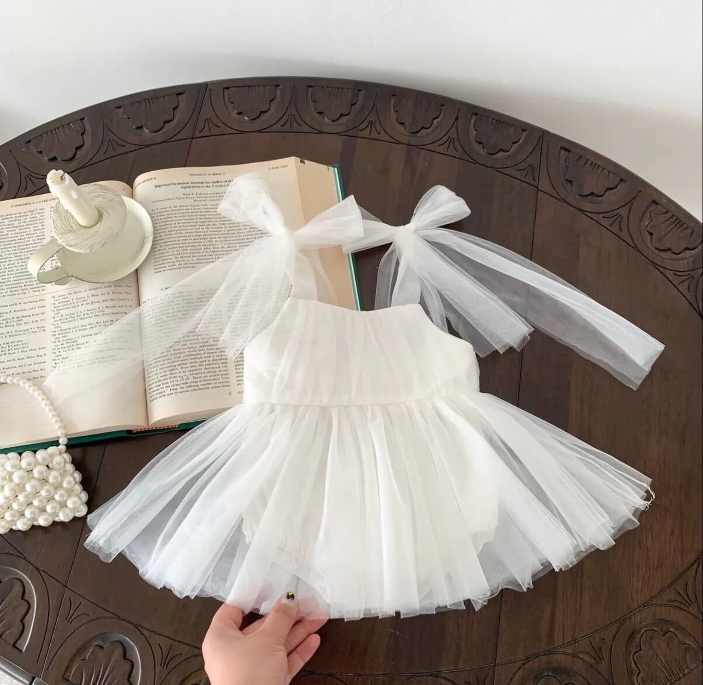 White tulle tutu dress with flared layered skirt displayed on dark wooden table with satin bow details.