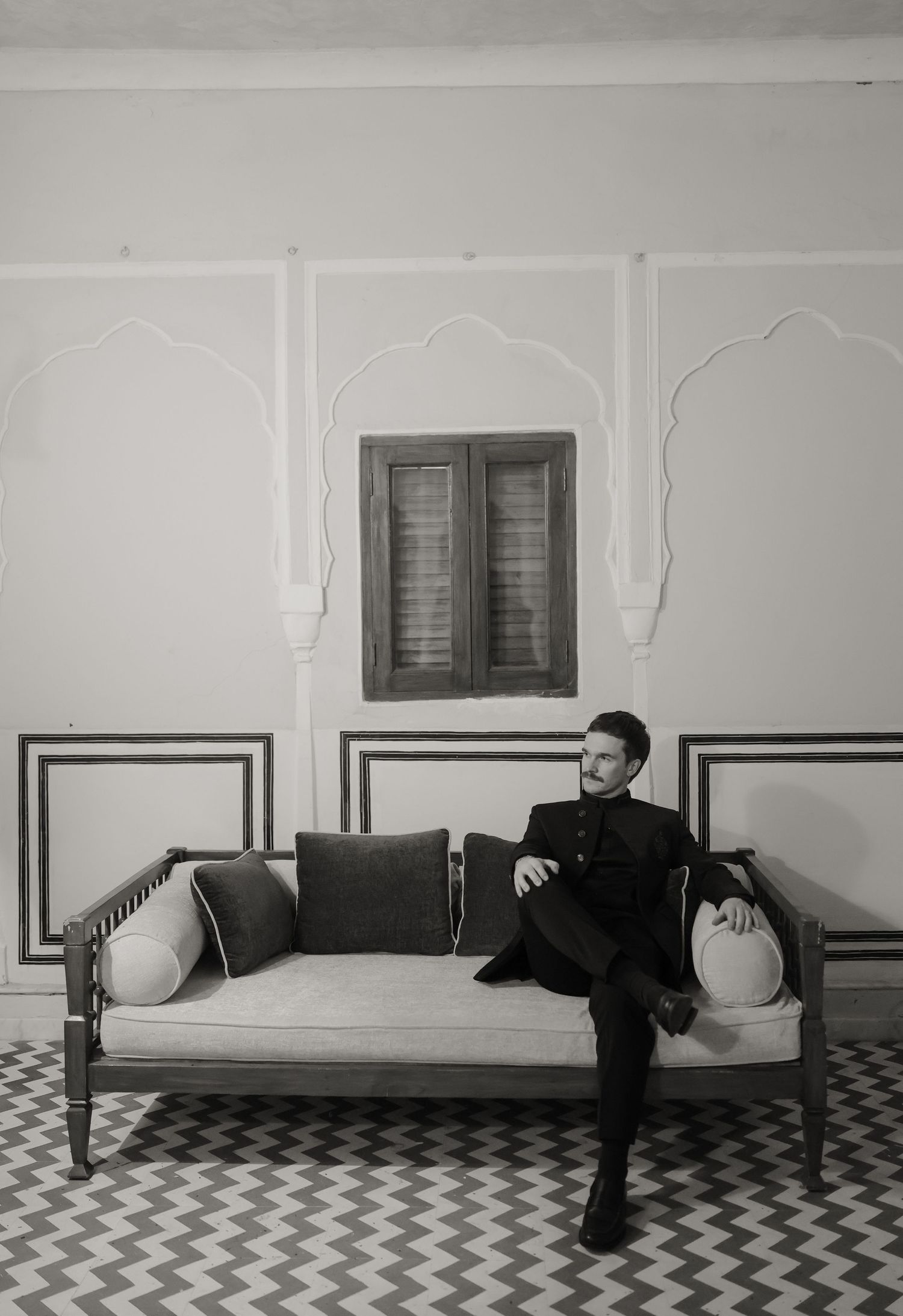 A black and white photo series showing a figure in dark clothing moving across a checkered floor against white walls.