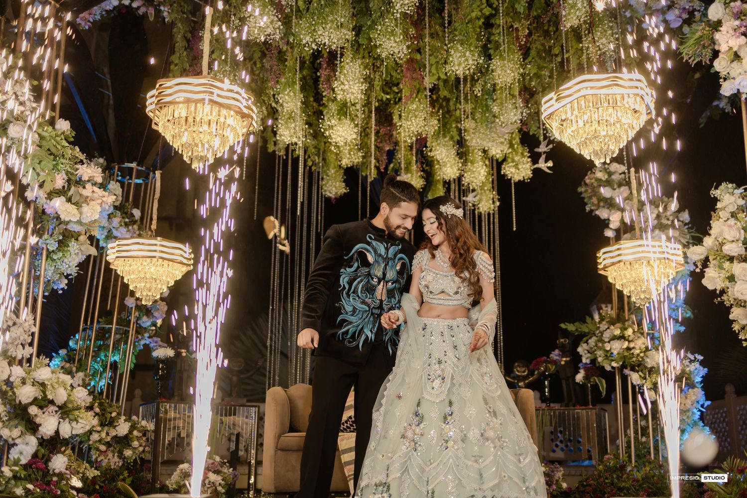Bride and groom share a romantic moment under chandelier and floral decor at an Indian wedding reception.