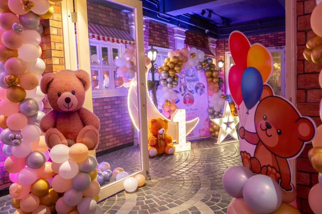 Teddy bear first birthday party decoration with colorful balloons, large plush bears, and number one display.